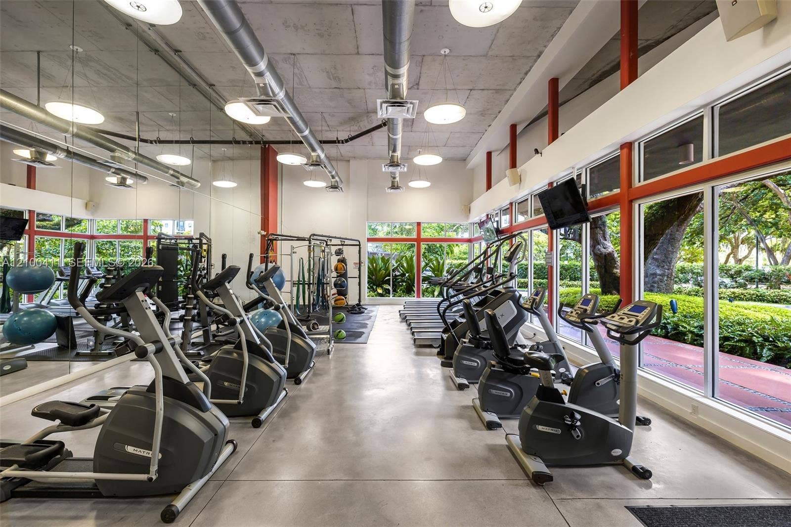 Industrial-style fitness space featuring exposed ductwork, concrete ceiling, concrete flooring, floor-to-ceiling windows with metal framing, and wall-to-wall mirrored surfaces