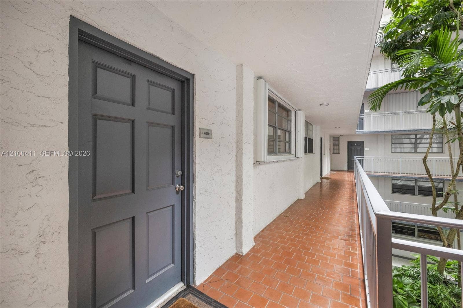 Exterior entryway featuring a textured stucco facade, a six-panel door, terracotta tile flooring, and a metal railing