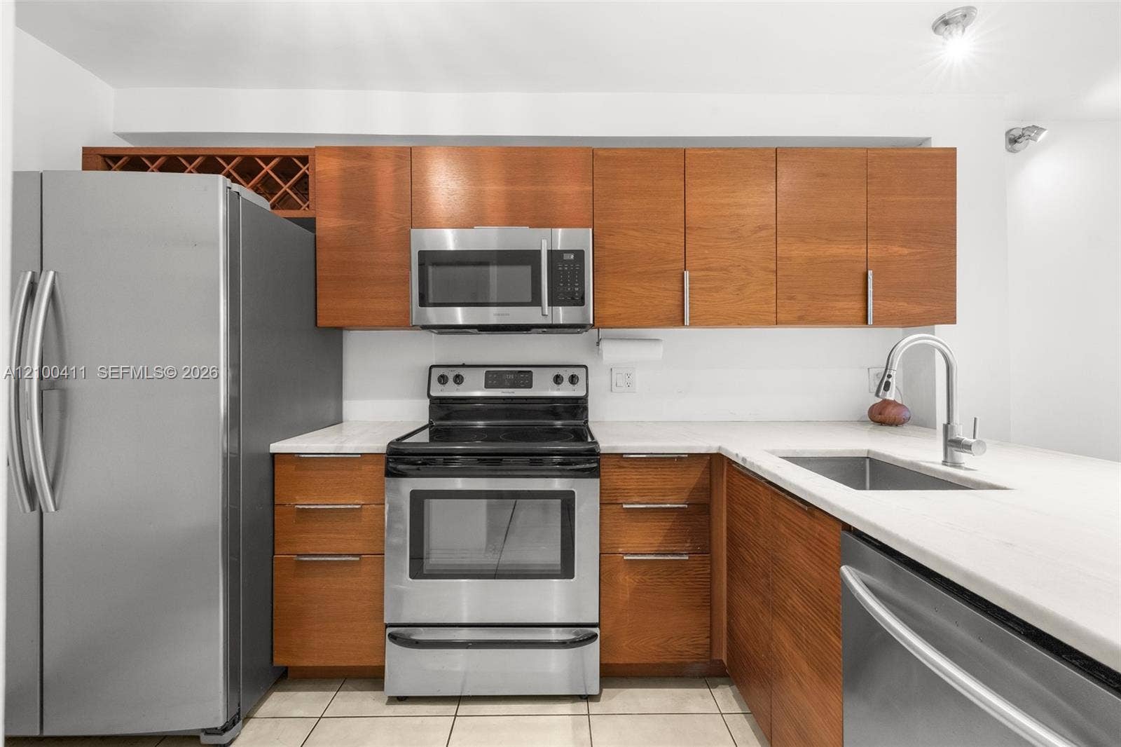 Kitchen featuring wood-finish cabinetry, built-in wine storage, stone-finish countertops, stainless steel appliances, and a stainless steel undermount sink with a gooseneck faucet