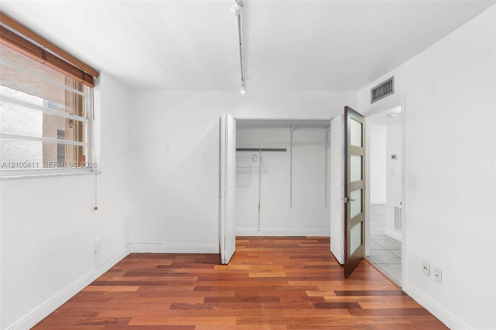Wood-finish flooring, multi-pane window with wood-trim surround, bi-fold closet doors with integrated shelving, and a glass-paneled interior door