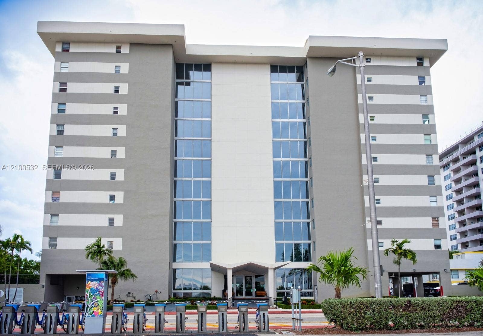9273 Collins Avenue, #912, Surfside, Surfside, FL 33154 Multi-story mid-century modern architectural design featuring a central glass curtain wall, flat roofline, and contrasting horizontal facade panels