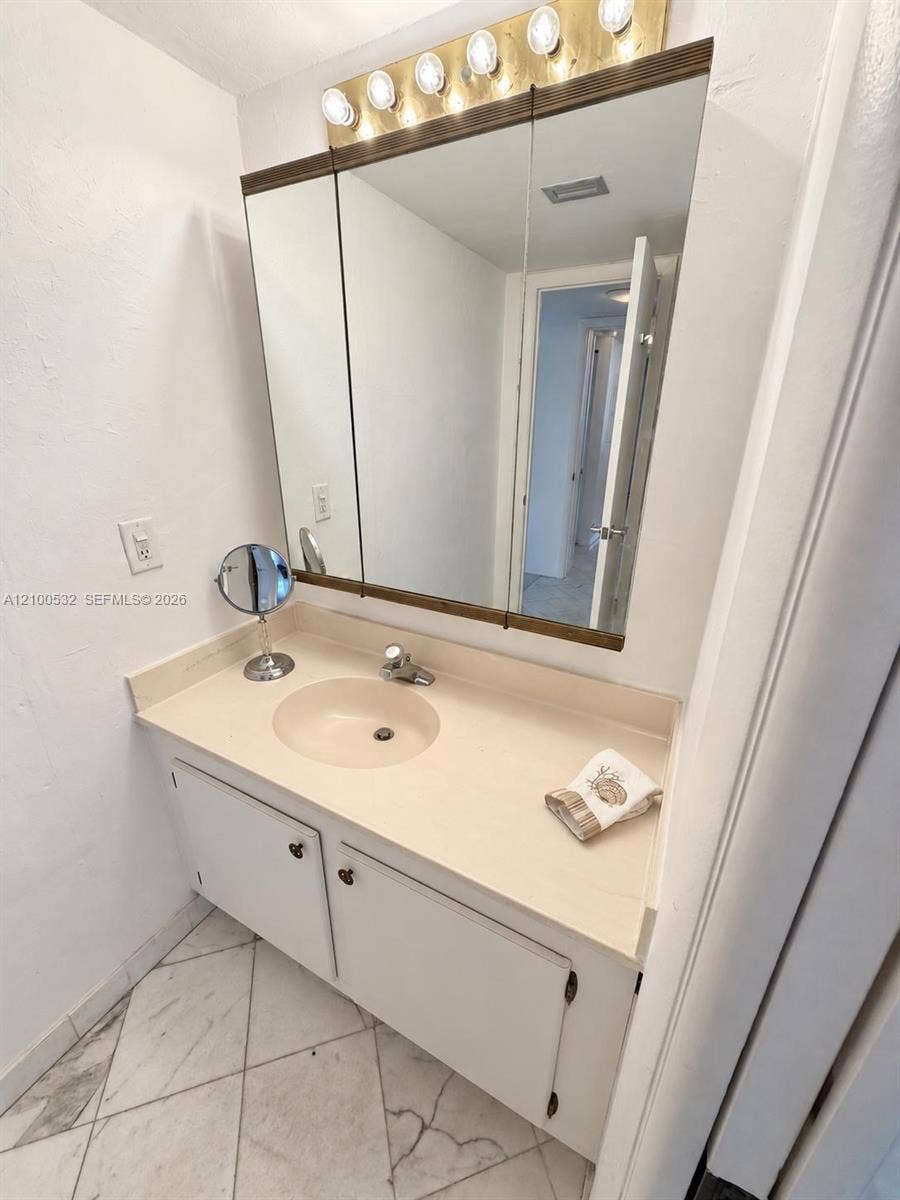 9273 Collins Avenue, #912, Surfside, Surfside, FL 33154 Vanity featuring a solid surface countertop with an integrated sink, three-panel medicine cabinet, five-bulb light fixture, and stone-finish tile flooring