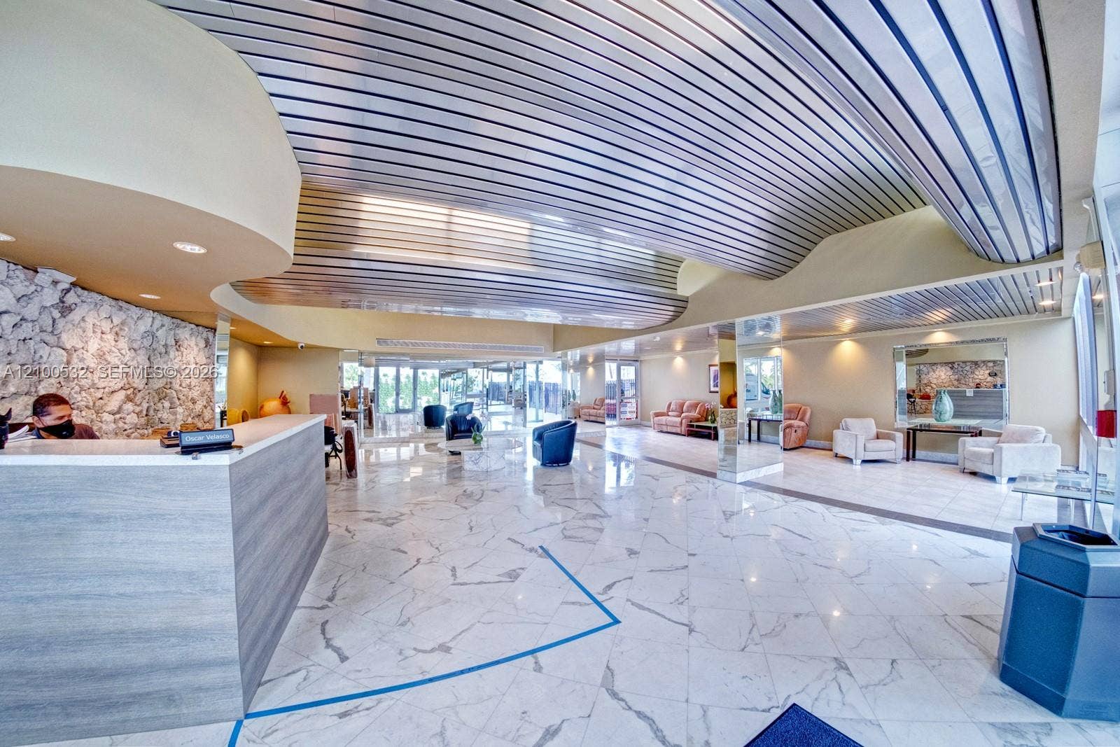 9273 Collins Avenue, #912, Surfside, Surfside, FL 33154 Spacious interior featuring a metallic corrugated ceiling, polished stone flooring, a large reception desk with wood-finish paneling, and an accent wall composed of natural stone