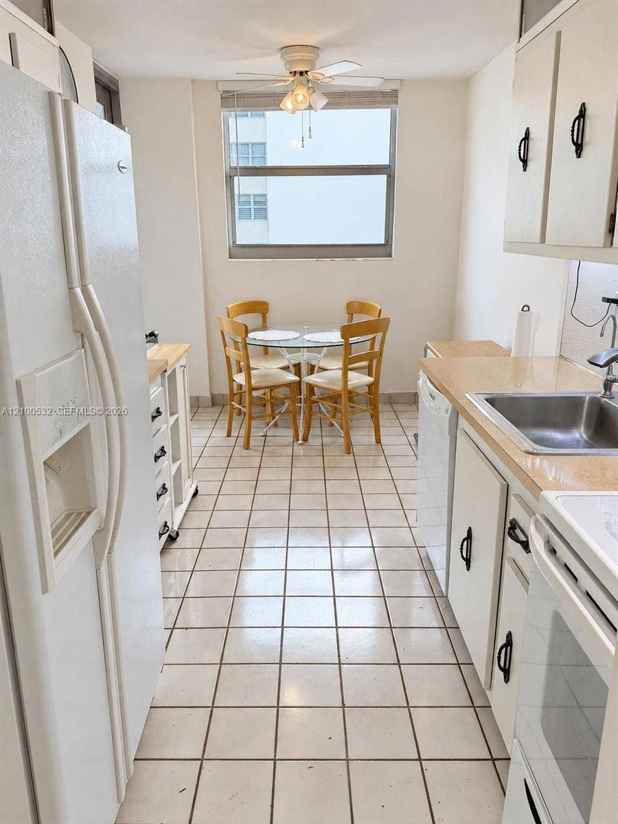 9273 Collins Avenue, #912, Surfside, Surfside, FL 33154 Galley kitchen featuring white cabinetry, light-toned countertops, ceramic tile flooring, a built-in stainless steel sink, and a ceiling-mounted light fixture