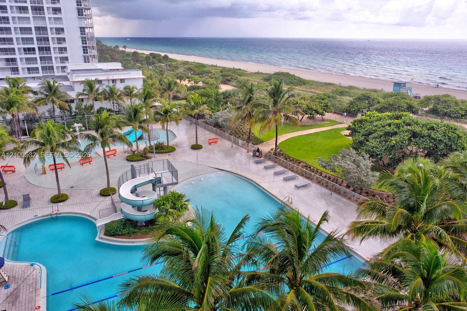 9273 Collins Avenue, #912, Surfside, Surfside, FL 33154 Outdoor swimming area featuring multiple pools, a water slide, expansive paved deck, and mature palm trees