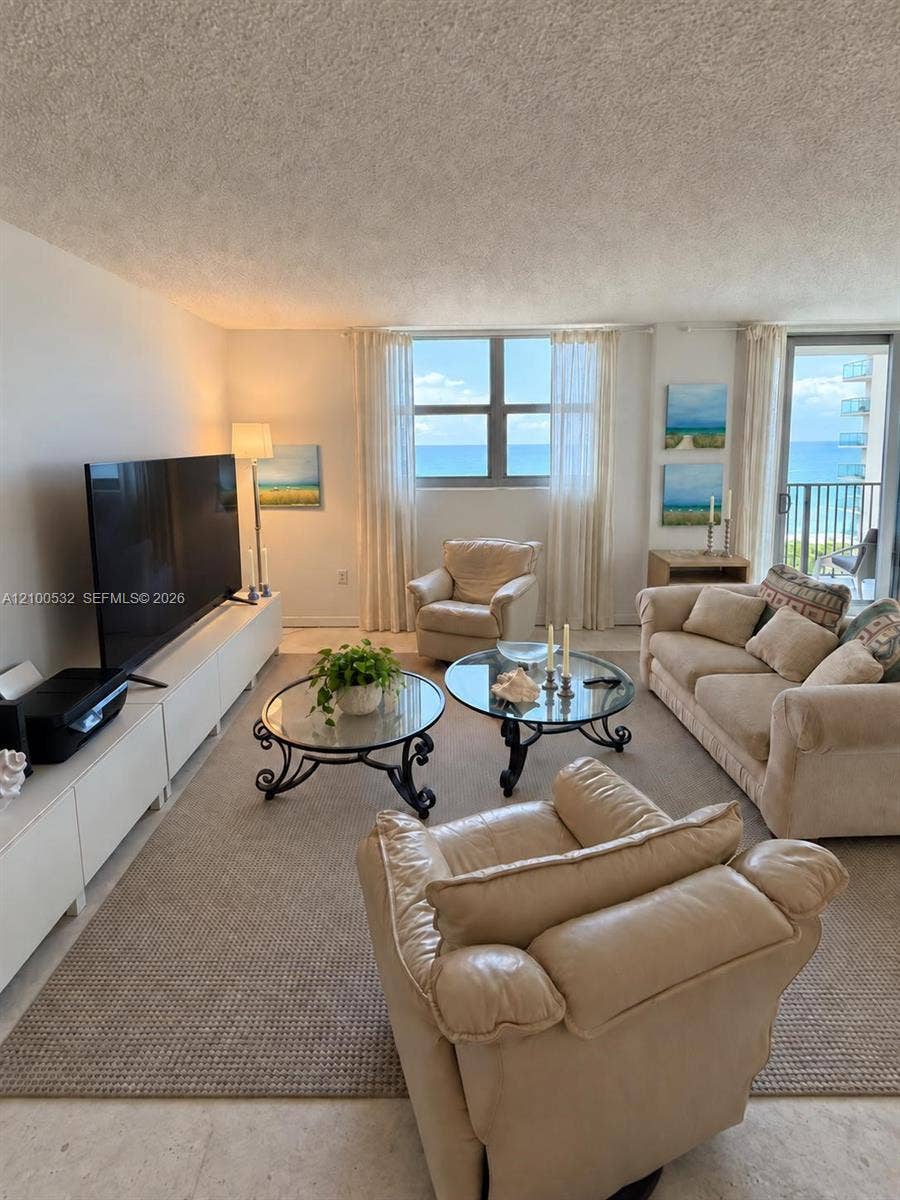 9273 Collins Avenue, #912, Surfside, Surfside, FL 33154 Living area featuring large windows, integrated storage cabinetry, neutral wall-to-wall carpeting, and a glass sliding door providing access to a balcony with ocean exposure