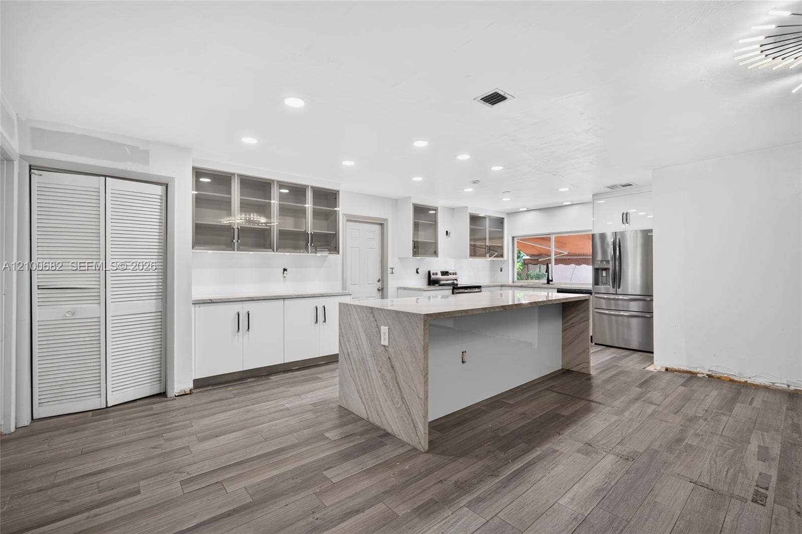 8402 SW 102nd Court, Miami, FL 33173 Kitchen featuring vinyl plank wood flooring, quartz-surfaced countertops and taj majal island with waterfall edge, white cabinetry, glass-front upper cabinets, and recessed ceiling lighting