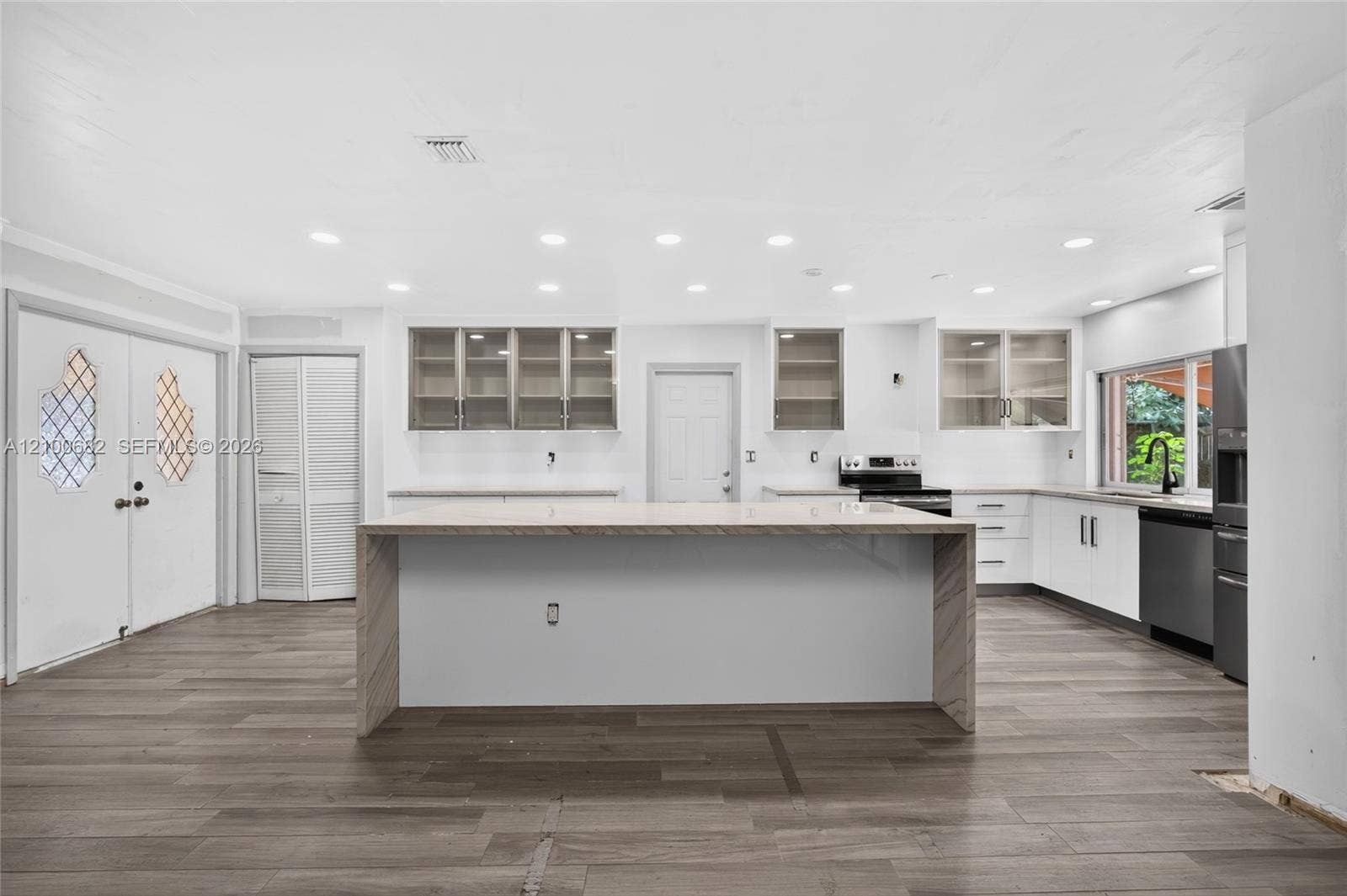 8402 SW 102nd Court, Miami, FL 33173 Kitchen featuring a waterfall-edge center island, vinly wood-finish flooring, white cabinetry with glass-front uppers, recessed lighting, and stainless steel appliances
