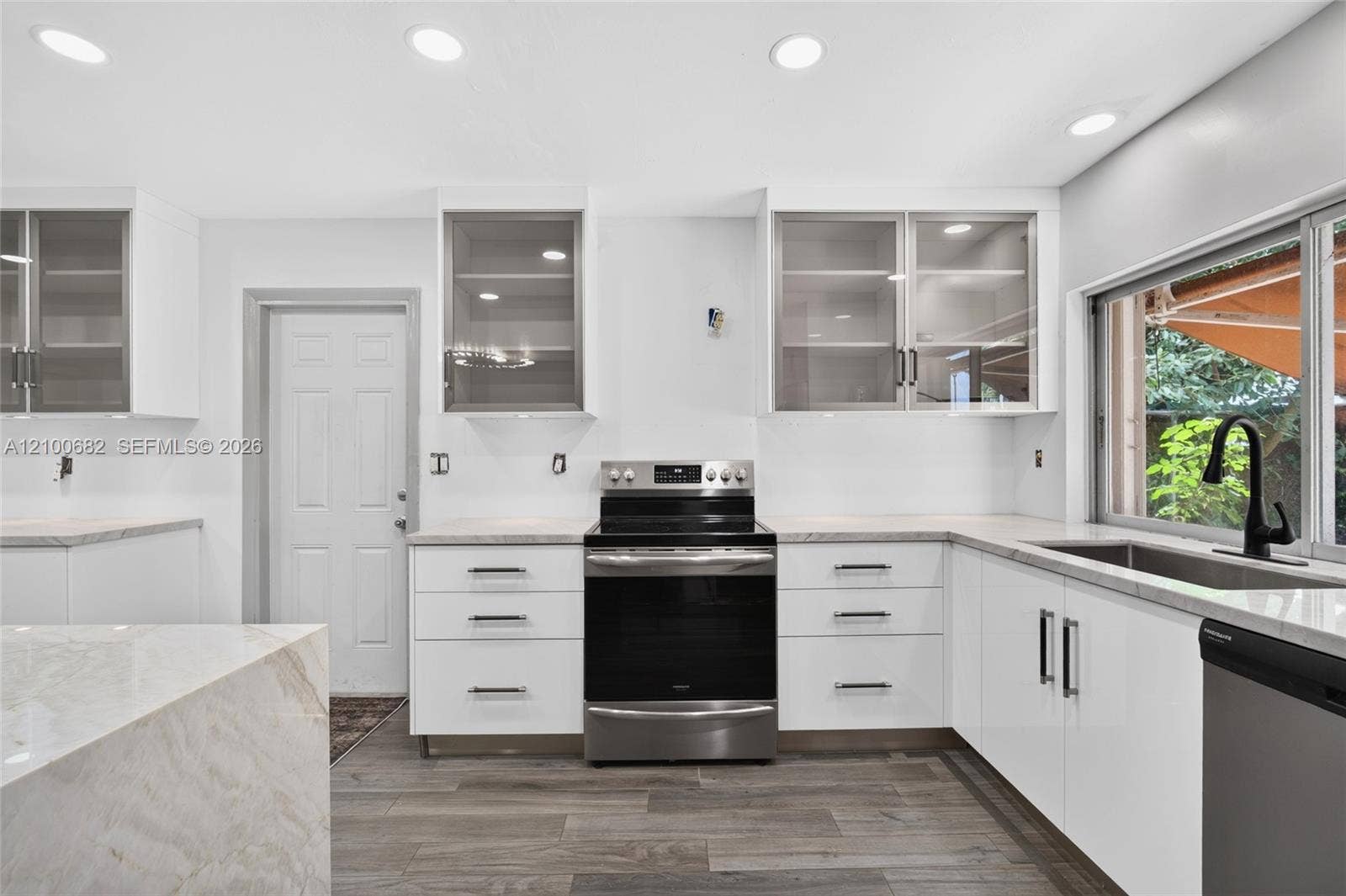 8402 SW 102nd Court, Miami, FL 33173 Kitchen featuring white cabinetry with glass-front uppers, solid surface countertops, stainless steel appliances, recessed lighting, and vinyl wood-finish flooring