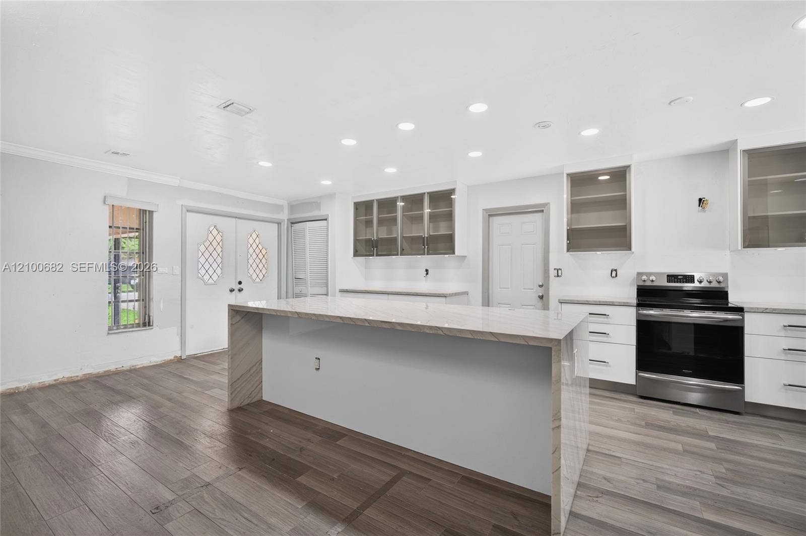 8402 SW 102nd Court, Miami, FL 33173 Kitchen featuring a waterfall-edge stone island, vinyl wood-finish flooring, white cabinetry, recessed lighting, and stainless steel range