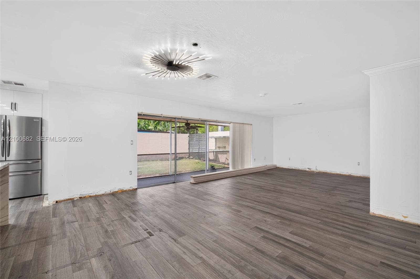 8402 SW 102nd Court, Miami, FL 33173 Open-concept interior featuring vinyl wood-finish flooring, a modern starburst-style ceiling light fixture, and large sliding glass doors to the covered patio*