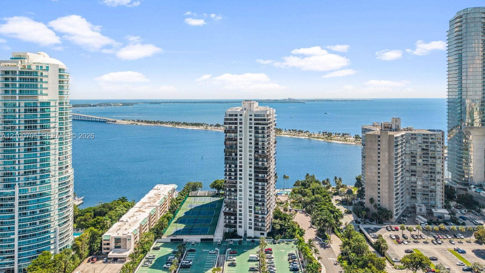 High-altitude perspective featuring expansive water and causeway scenery, tennis courts, and mature landscaping