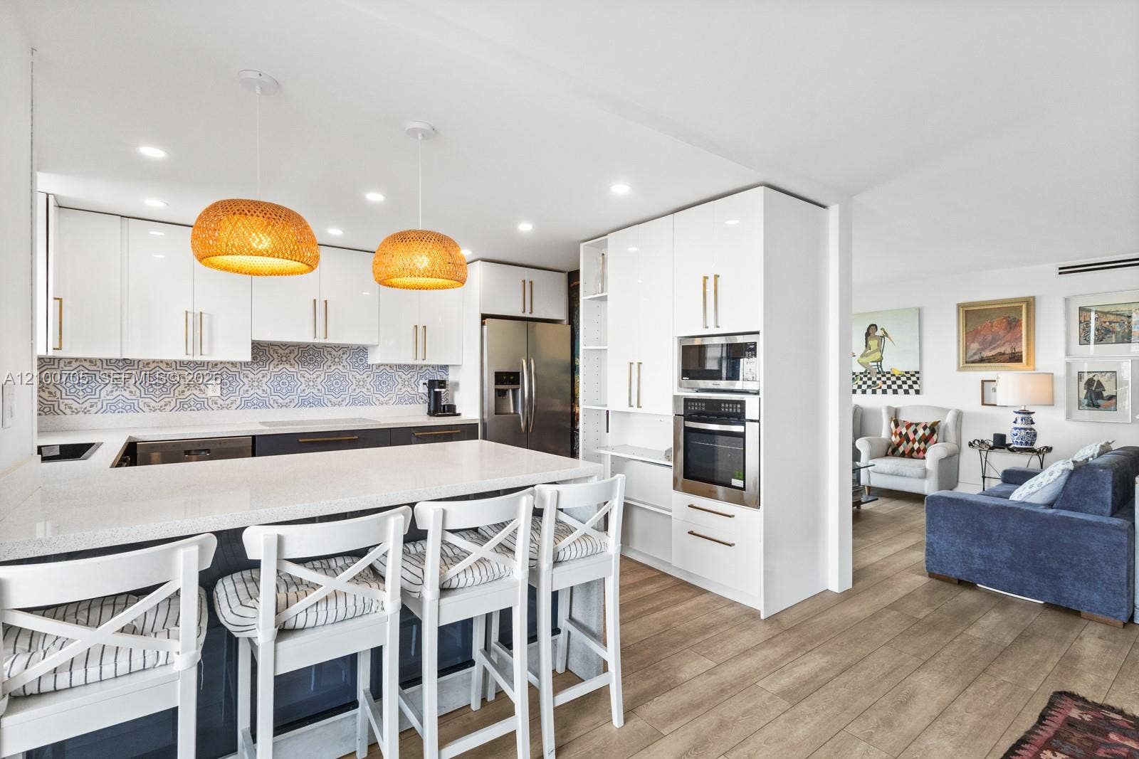 Kitchen featuring high-gloss white cabinetry, patterned tile backsplash, quartz-surfaced island, stainless steel built-in oven, and wood-finish flooring