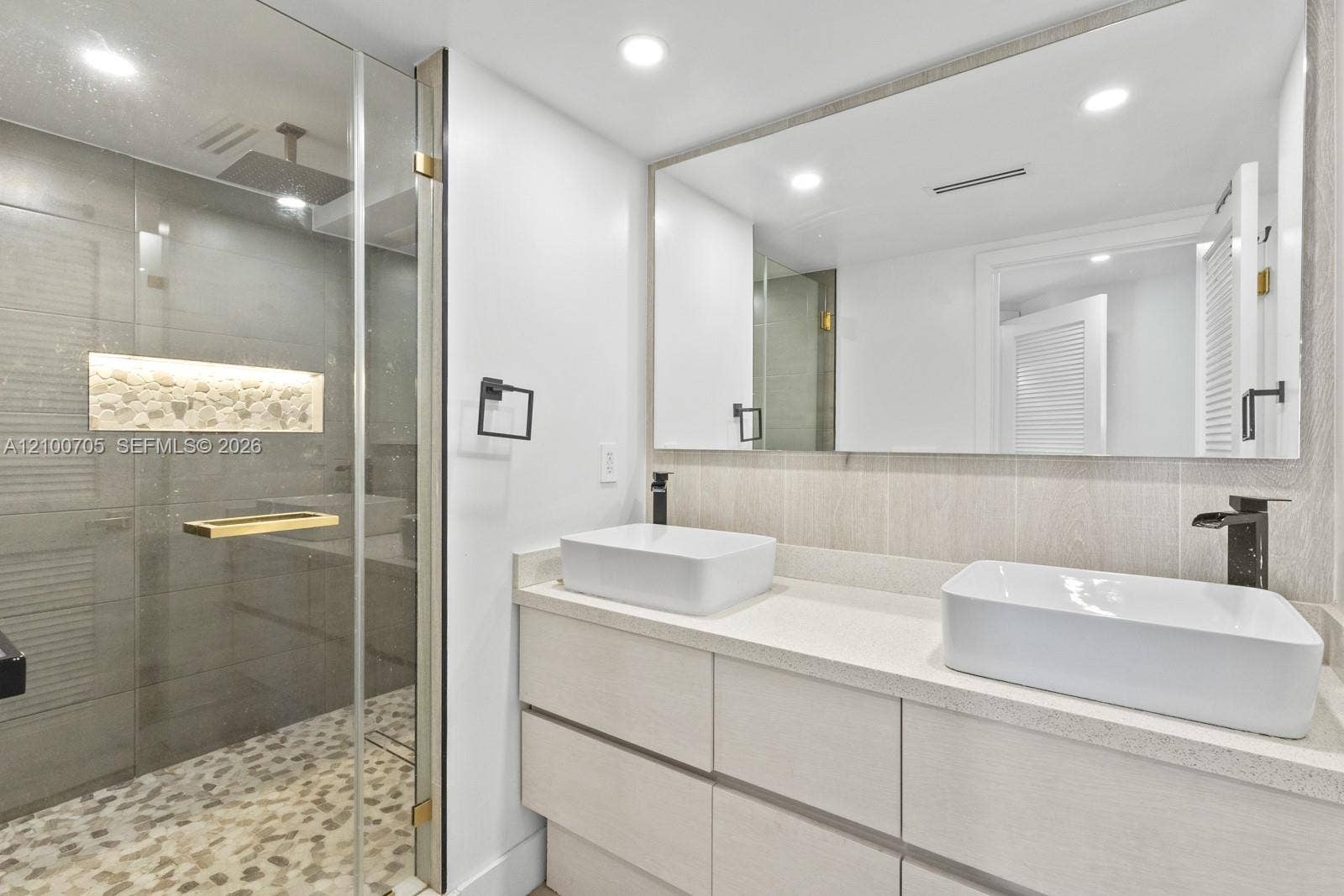 Double vanity featuring rectangular vessel sinks, stone-finish countertops, matte black fixtures, and a glass-enclosed shower with pebble tile flooring and a built-in stone niche