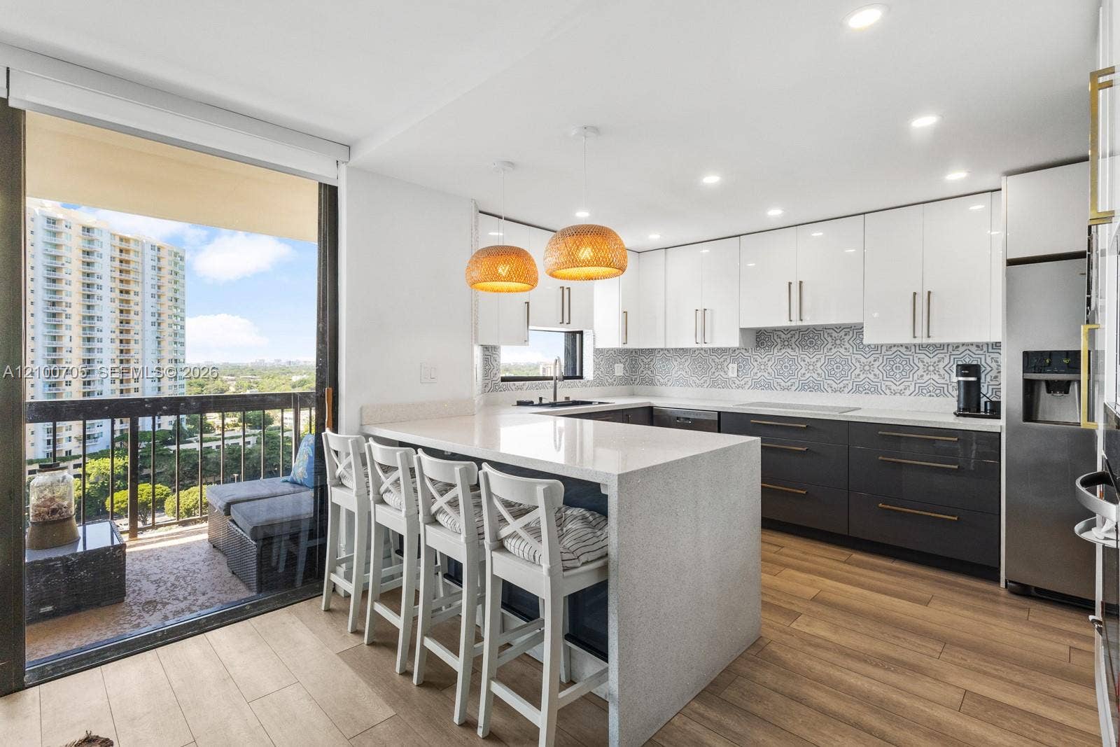 Kitchen featuring white upper cabinetry, dark lower cabinetry, quartz waterfall countertop island, patterned tile backsplash, and wood-finish flooring