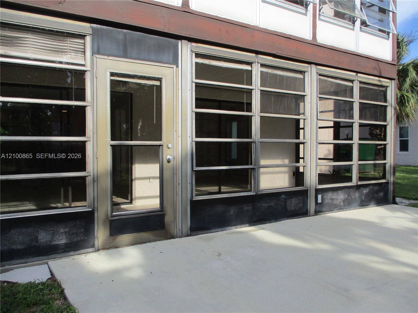 6531 SE Federal Highway, #J112, Stuart, FL 34997 Ground-level patio with a concrete surface, featuring multiple large glass panels, a full-light entry door, and upper-level awning windows
