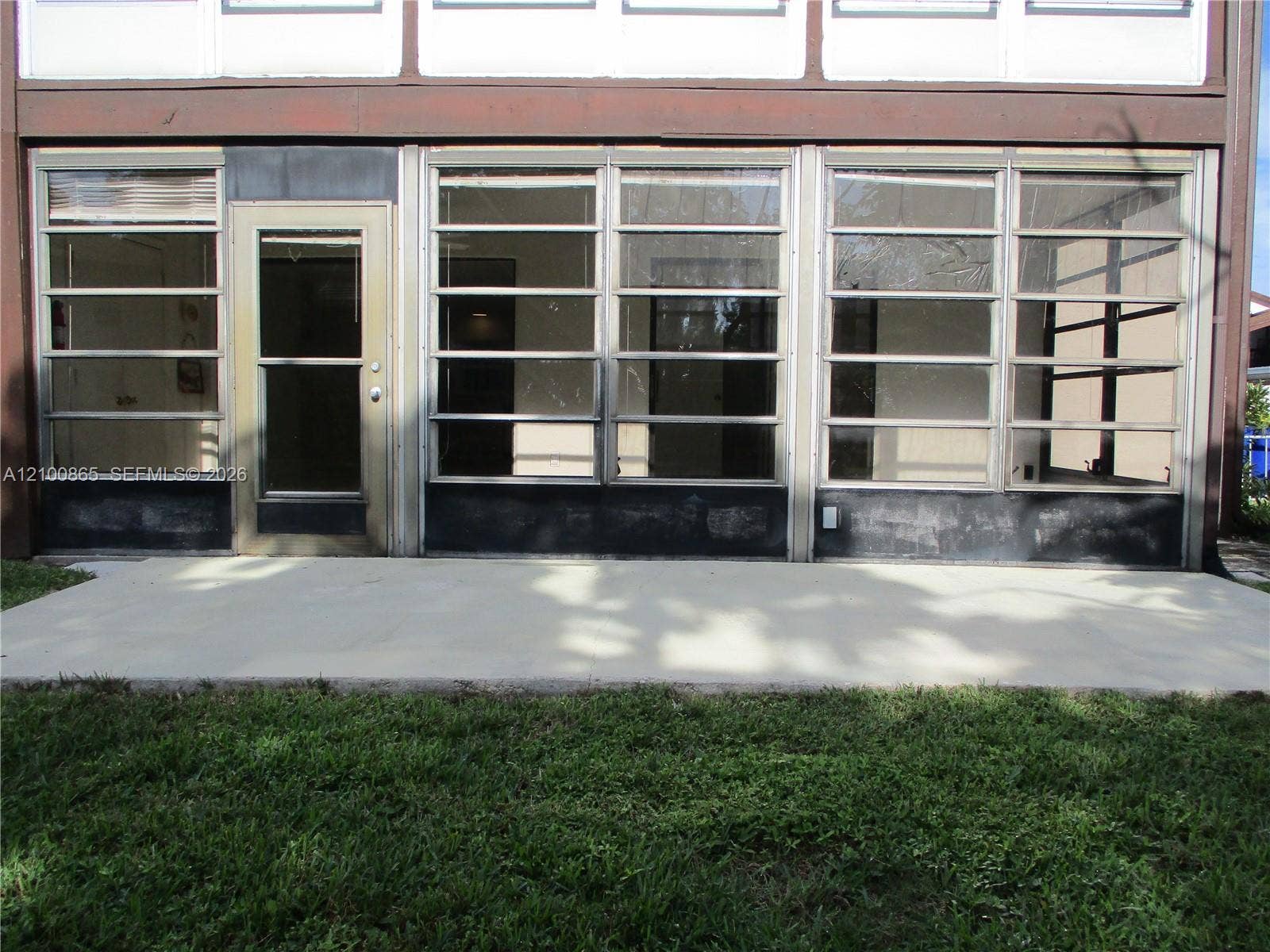 6531 SE Federal Highway, #J112, Stuart, FL 34997 Enclosed patio featuring a concrete slab foundation, multiple horizontal louvered windows, and a glass-paneled entry door