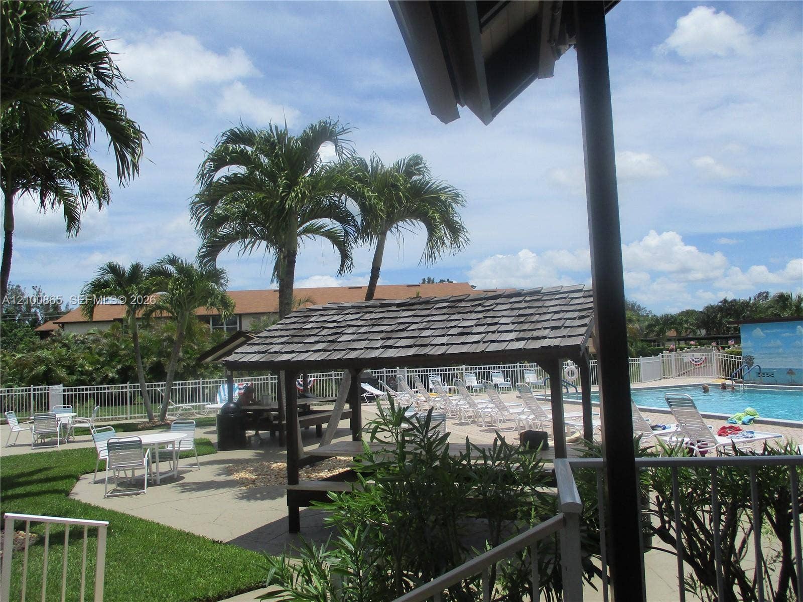 6531 SE Federal Highway, #J112, Stuart, FL 34997 Community swimming pool & picnic area, with concrete decking, wood-shingled gazebo, white metal fencing, and mature palm trees