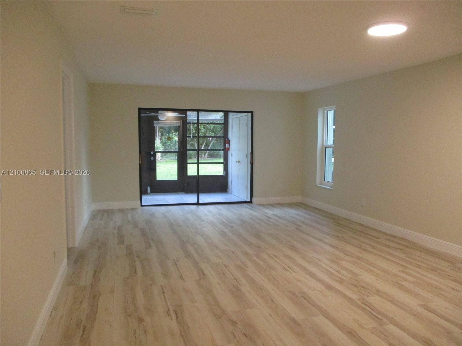 6531 SE Federal Highway, #J112, Stuart, FL 34997 Open-concept interior featuring light wood-finish flooring, recessed lighting, and large sliding glass doors with a black frame leading to a screened enclosure