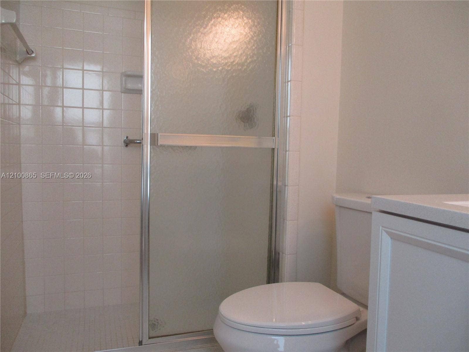 6531 SE Federal Highway, #J112, Stuart, FL 34997 Master bathroom Shower stall with white square wall tile, semi-frameless textured glass door, and built-in soap niche, paired with a white vanity and porcelain commode