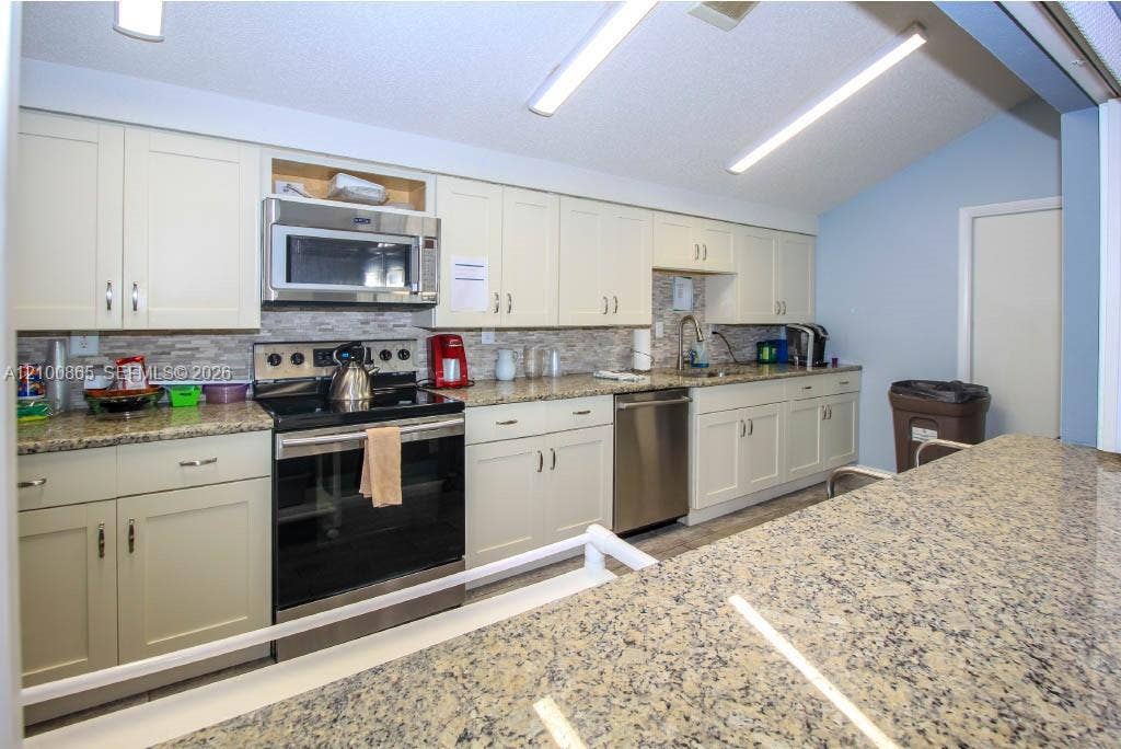 6531 SE Federal Highway, #J112, Stuart, FL 34997 Community Kitchen featuring cream-colored cabinetry, stone-patterned countertops, a stainless steel microwave and dishwasher, and a stone-tile backsplash