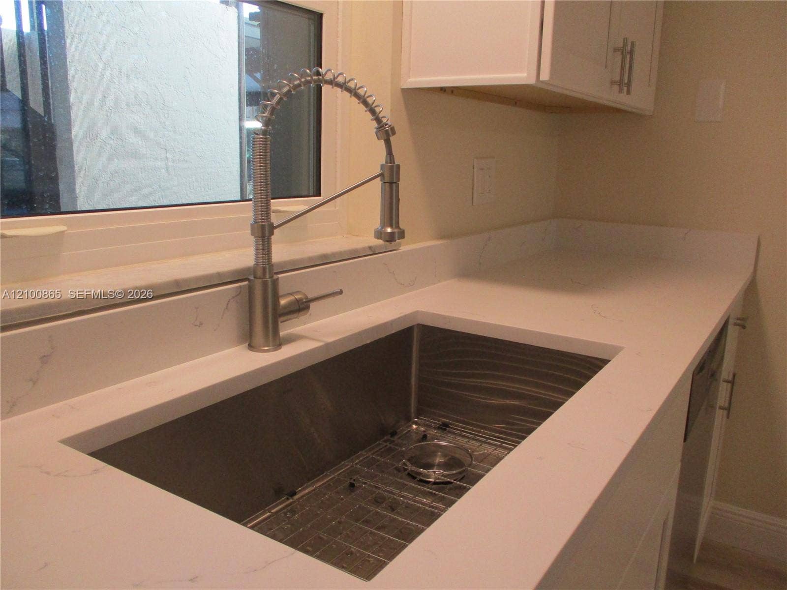 6531 SE Federal Highway, #J112, Stuart, FL 34997 Undermount stainless steel sink with a protective grid, high-arc brushed nickel spring-neck faucet, and white stone-composite countertops with veining detail