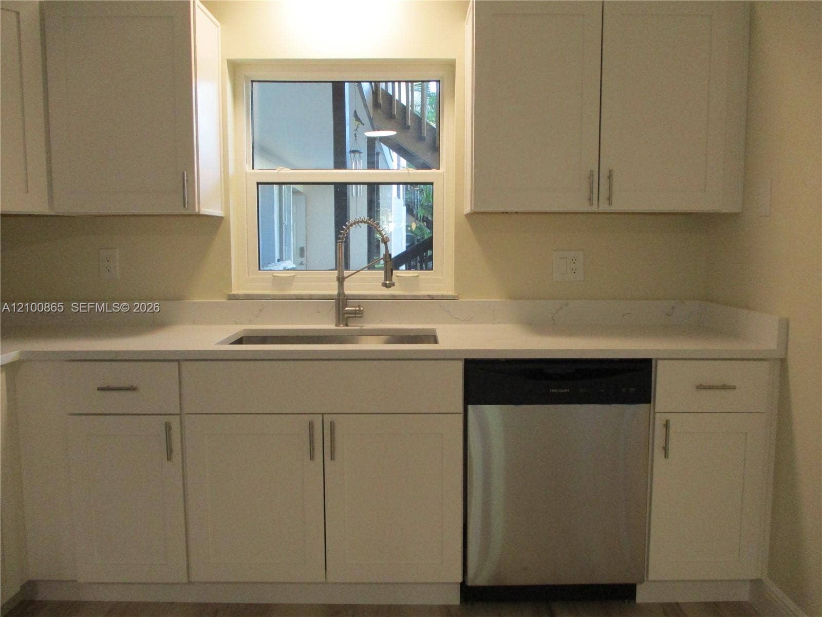6531 SE Federal Highway, #J112, Stuart, FL 34997 Kitchen featuring white shaker-style cabinetry, granite countertops, stainless steel undermount sink with a gooseneck faucet, and a stainless steel dishwasher