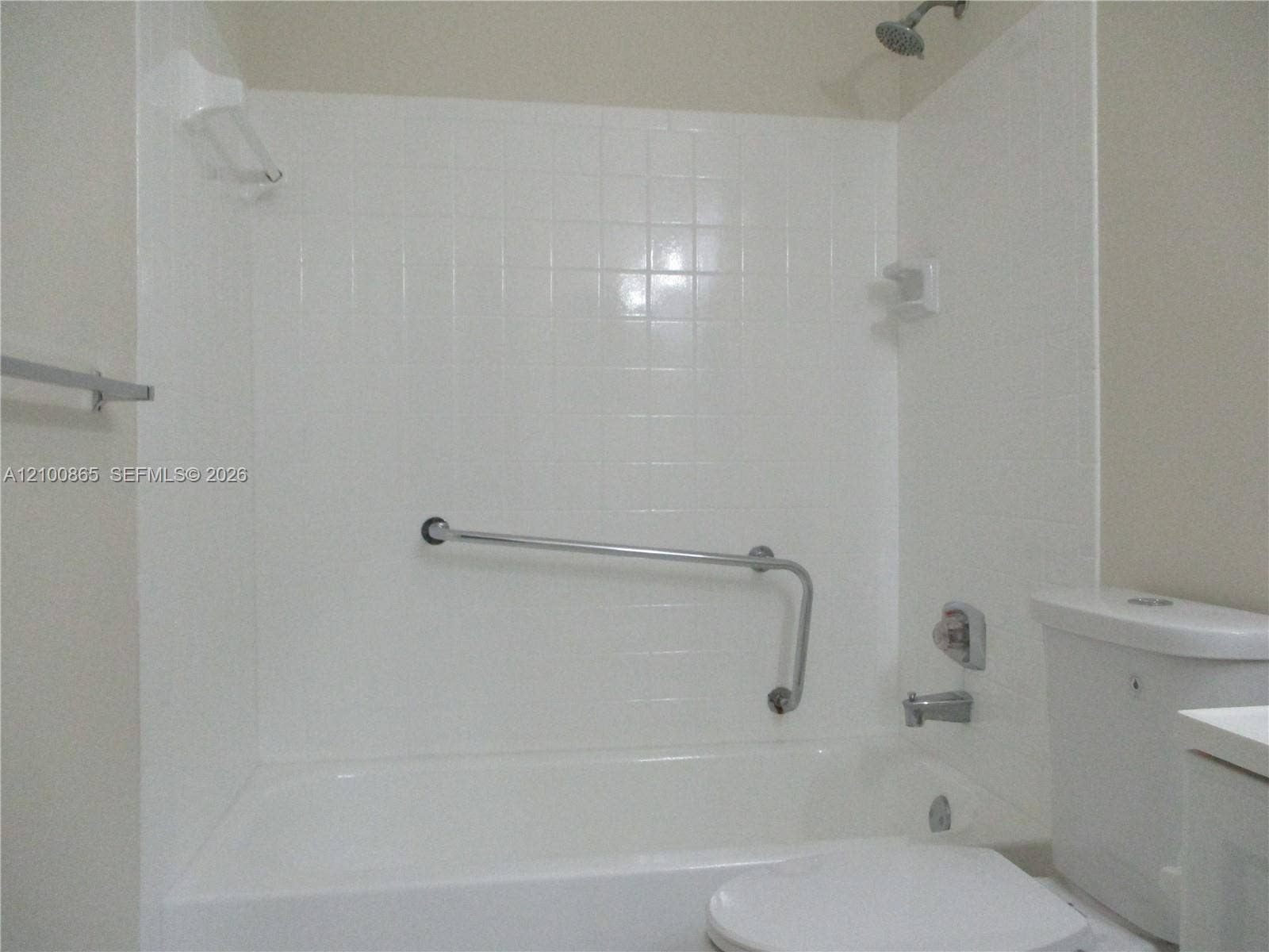 6531 SE Federal Highway, #J112, Stuart, FL 34997 Guest Bathtub enclosure featuring white ceramic wall tiles, a built-in soap dish, a wall-mounted metal grab bar, and a standard metal shower head and faucet fixture