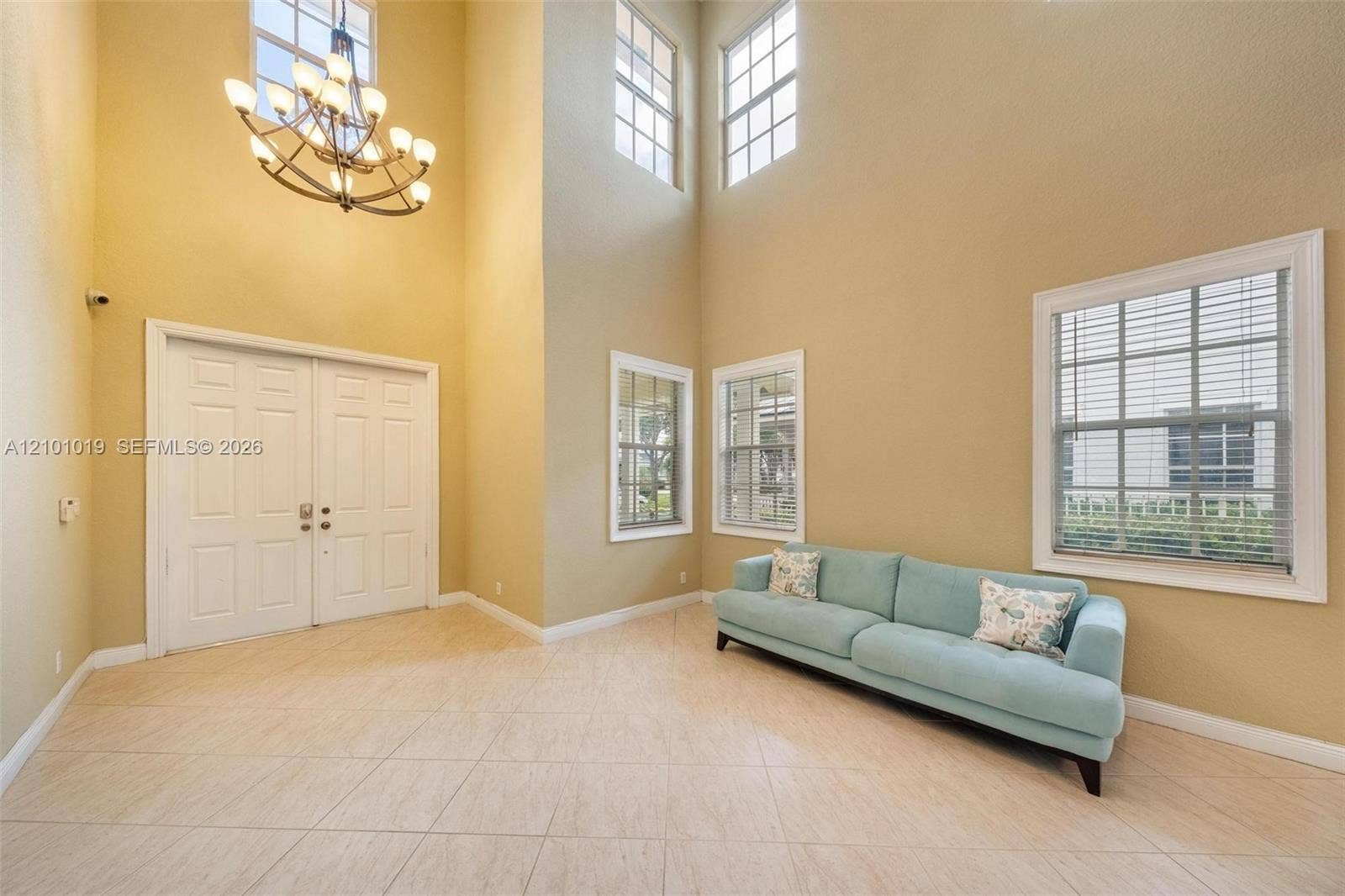 Double-height ceilings featuring an iron chandelier, large multi-pane windows, and neutral tile flooring