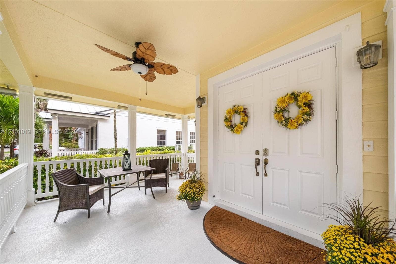 Covered front porch featuring a ceiling fan with leaf-style blades, painted white columns, a white balustrade railing, and double entry doors