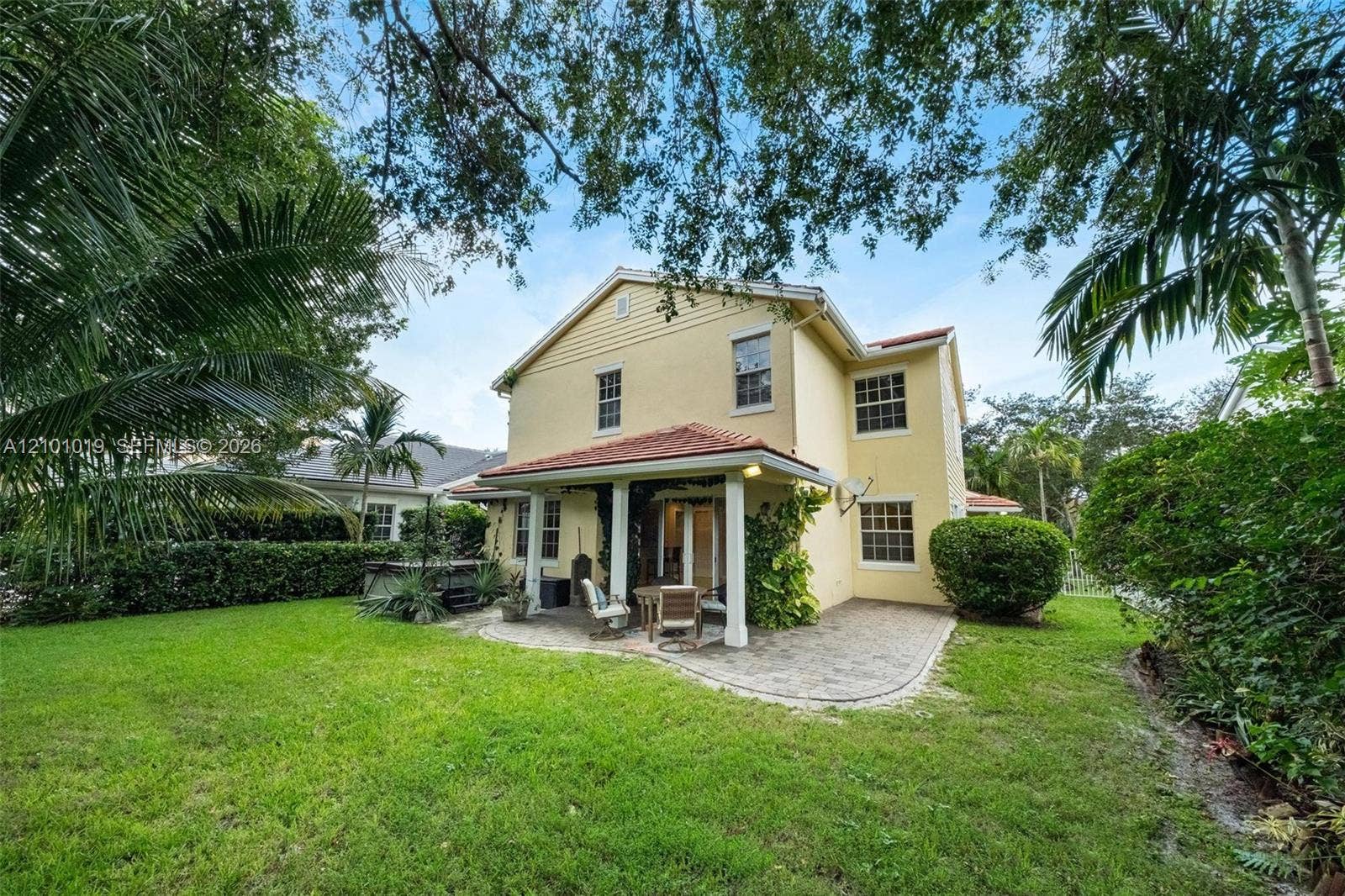 Stucco exterior featuring a covered patio with concrete pavers, a tile roof, mature landscaping, and an expansive lawn