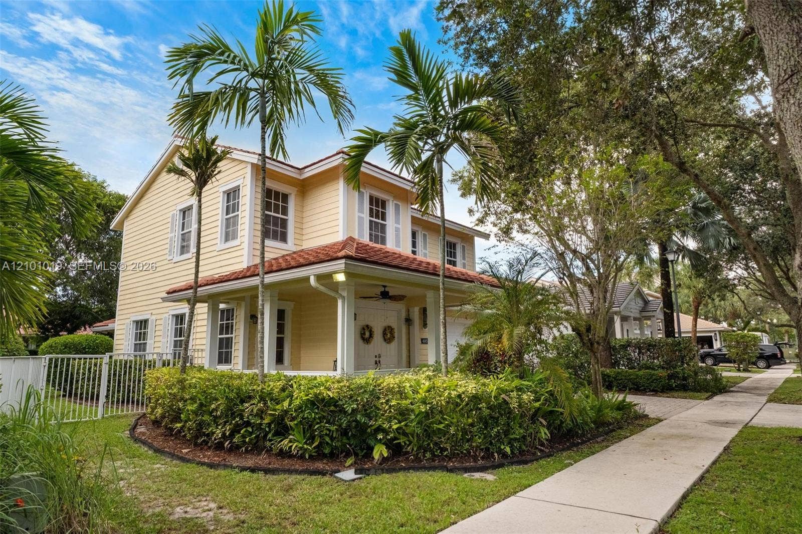 Two-story exterior featuring light yellow horizontal siding, a tiled roof, a covered front porch, and manicured landscaping