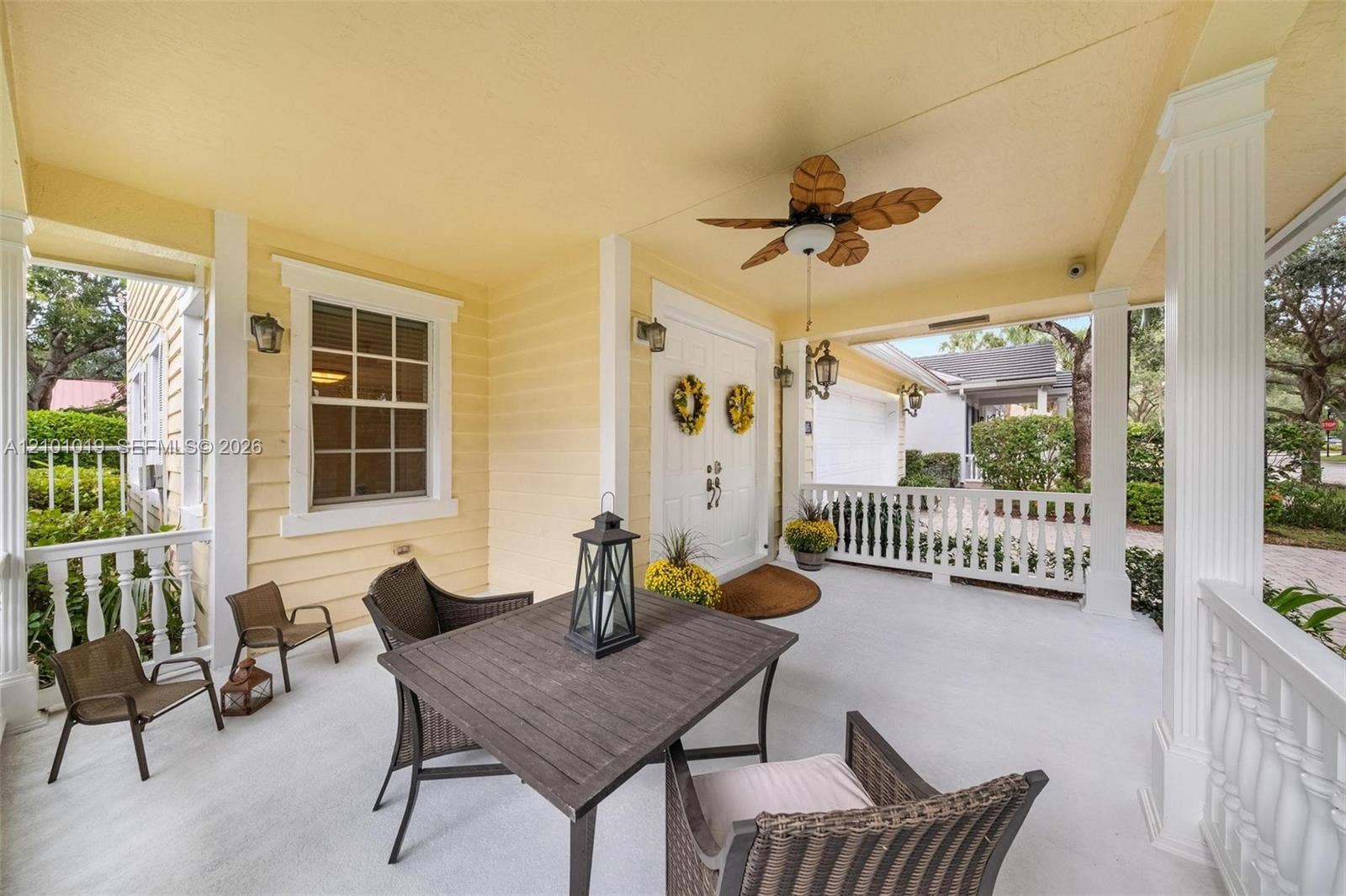 Covered front porch featuring white railings, structural columns, a ceiling-mounted fan, and double-entry doors