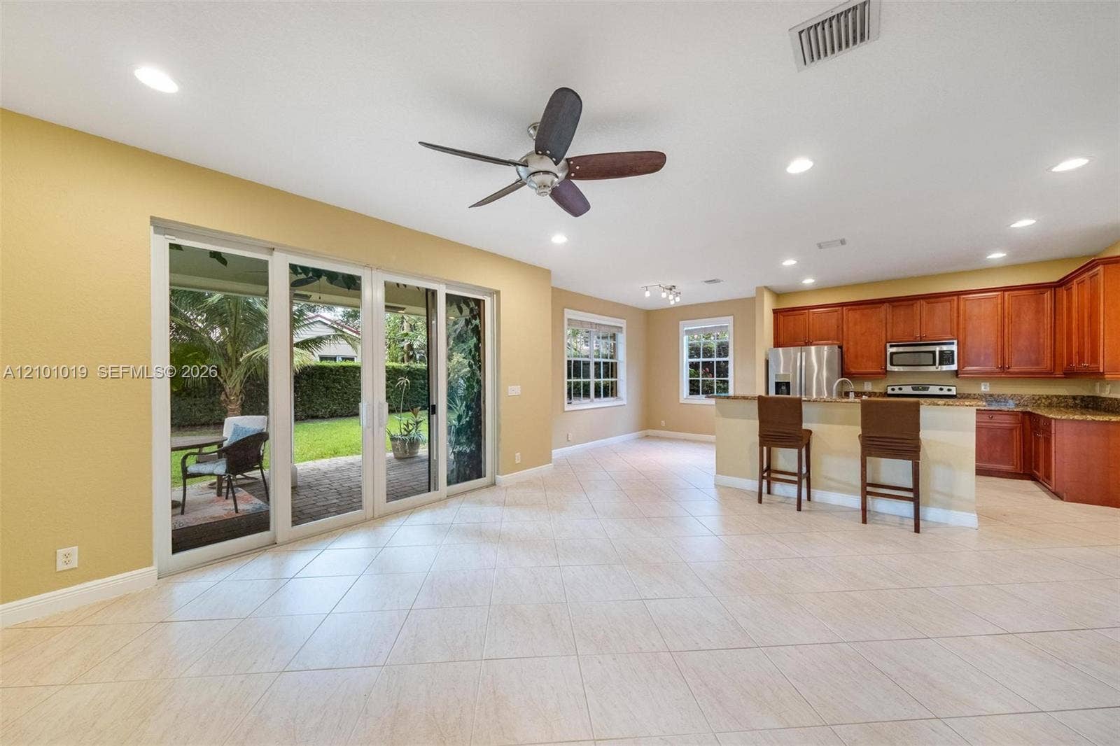 Open-concept area featuring tile flooring, recessed lighting, ceiling fan, sliding glass doors, and a kitchen equipped with wood cabinetry and stainless steel appliances