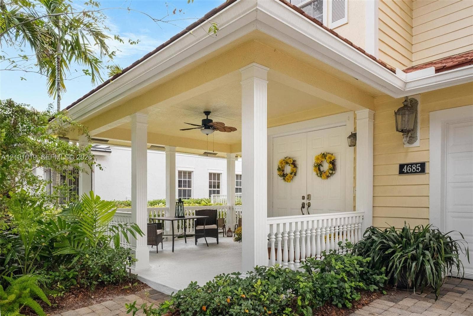 Covered entryway featuring a wrap-around porch with white balustrade railings, white columns, a ceiling-mounted fan, and double entry doors