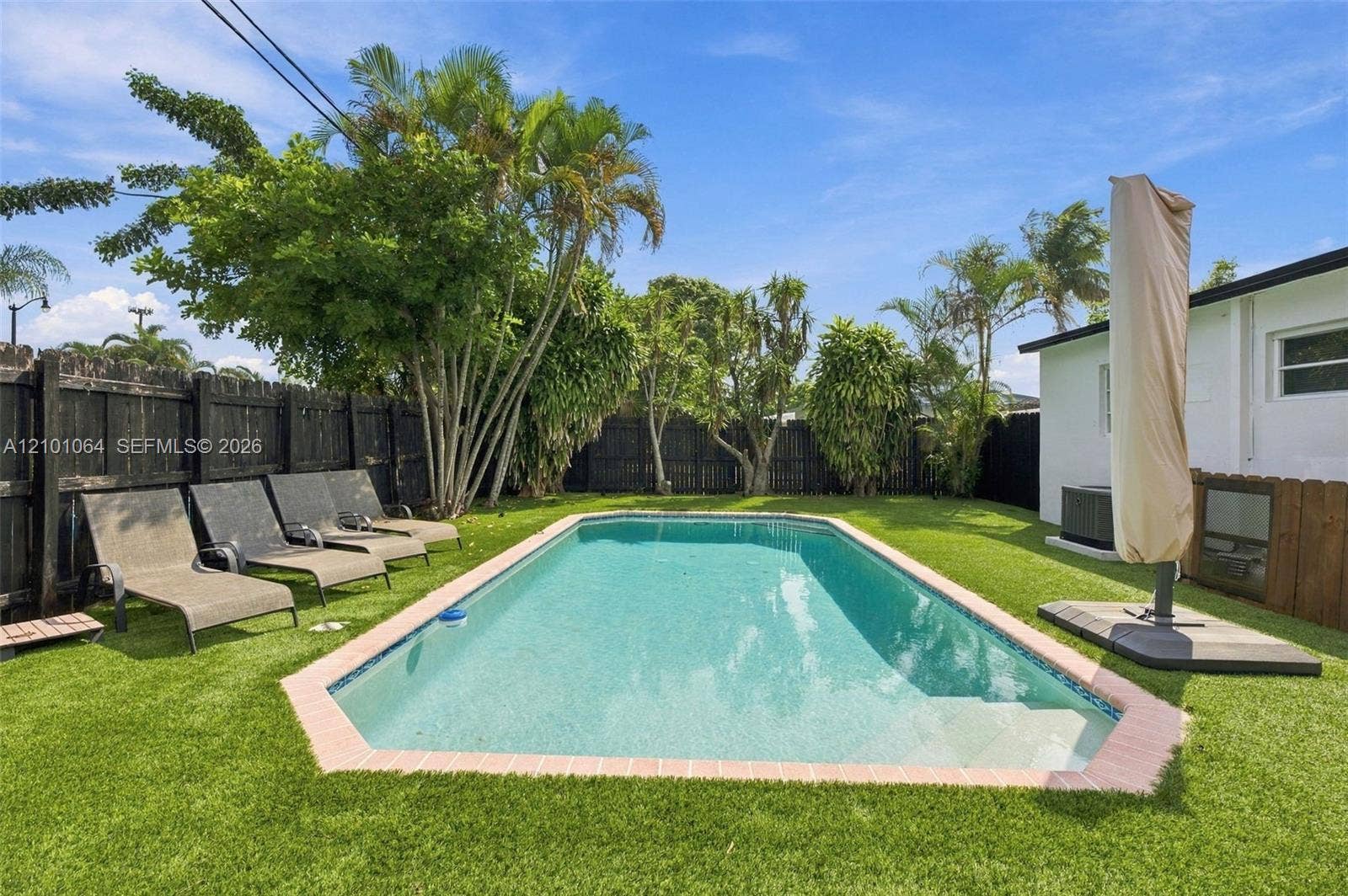 2632 NE 15th Avenue, Pompano Beach, FL 33064 Rectangular in-ground swimming pool featuring a brick-style coping, artificial turf lawn, and perimeter wood privacy fencing