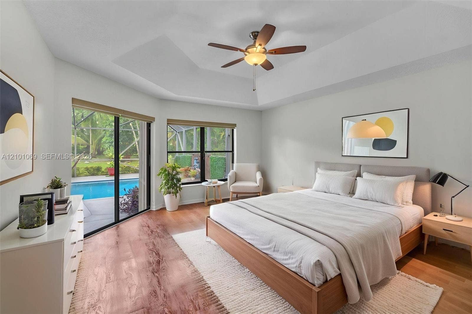 Master bedroom, tray ceiling, wood-finish flooring, and large sliding glass doors providing outdoor access-virtually staged