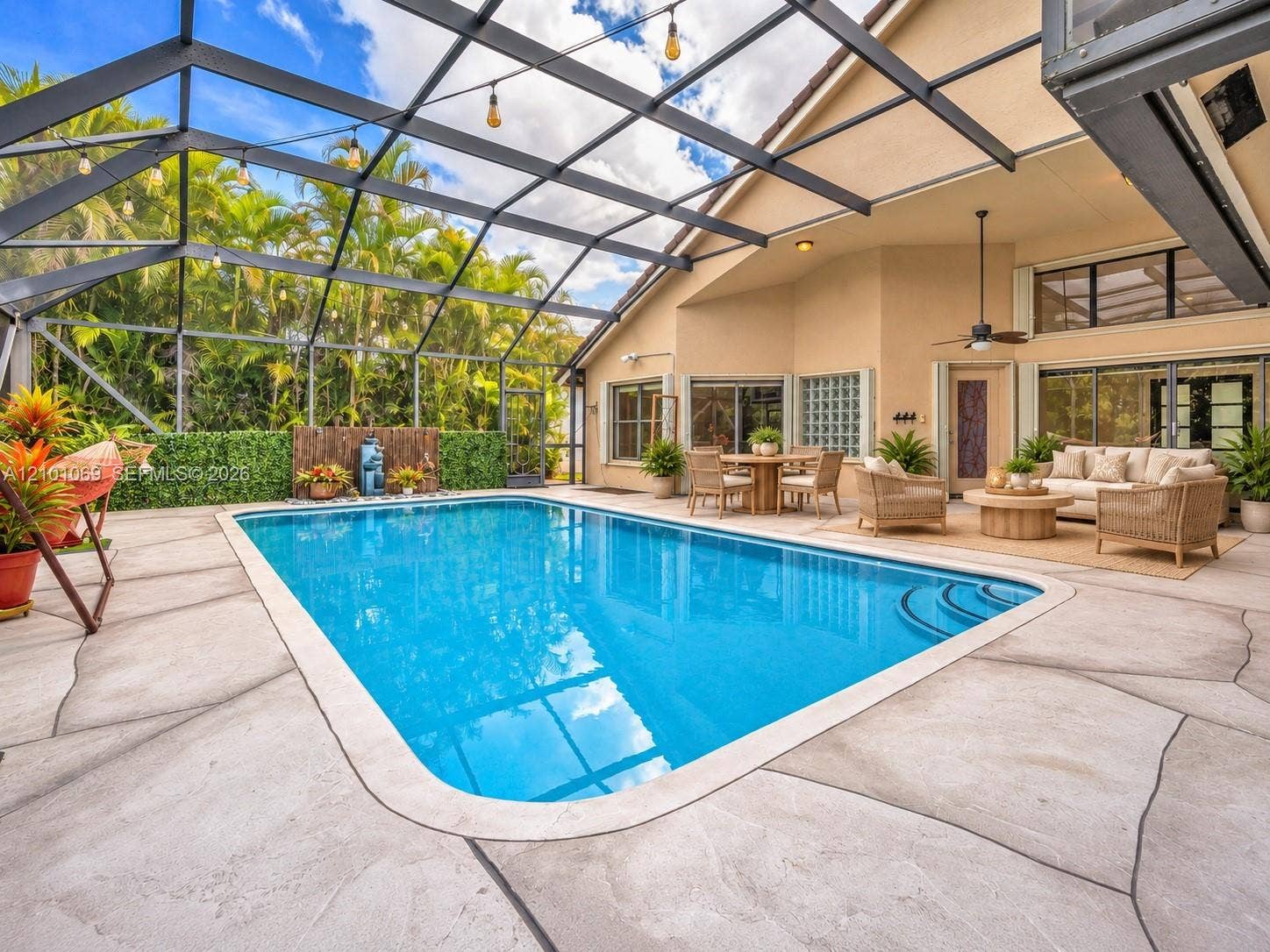 Screened-in outdoor living area featuring a custom-shaped swimming pool with built-in stairs, decorative concrete patio decking, and a ceiling fan