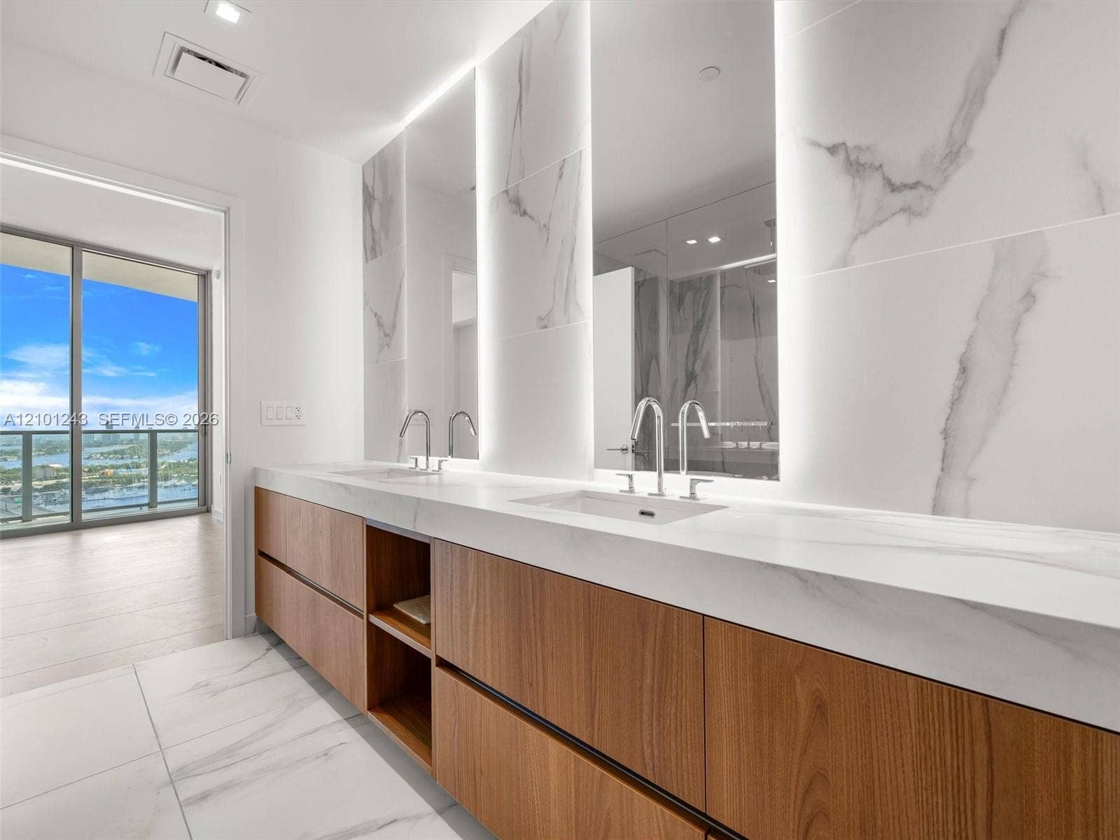 Floating wood-finish vanity with dual integrated sinks, light-toned stone-finish countertop, full-height decorative stone-finish backsplash, and recessed LED mirror lighting