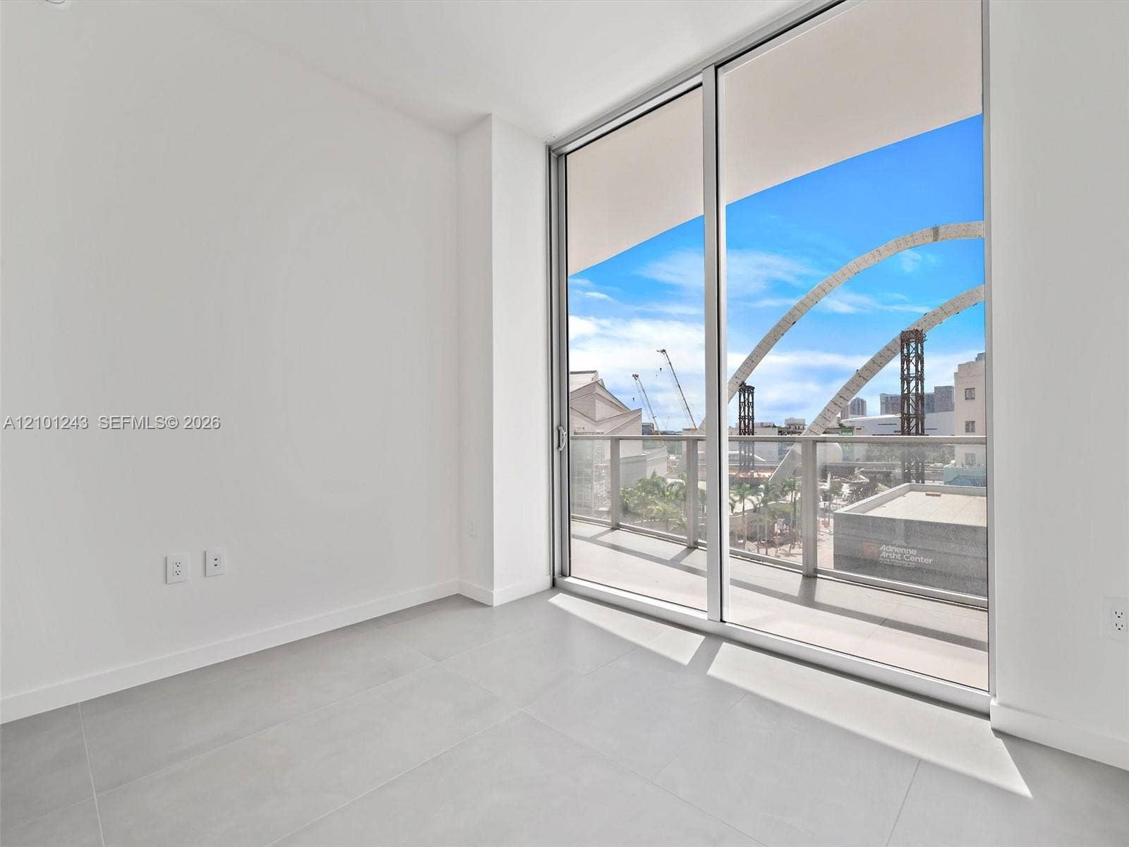 Floor-to-ceiling sliding glass doors, large format tile flooring, and a private balcony with a metal railing