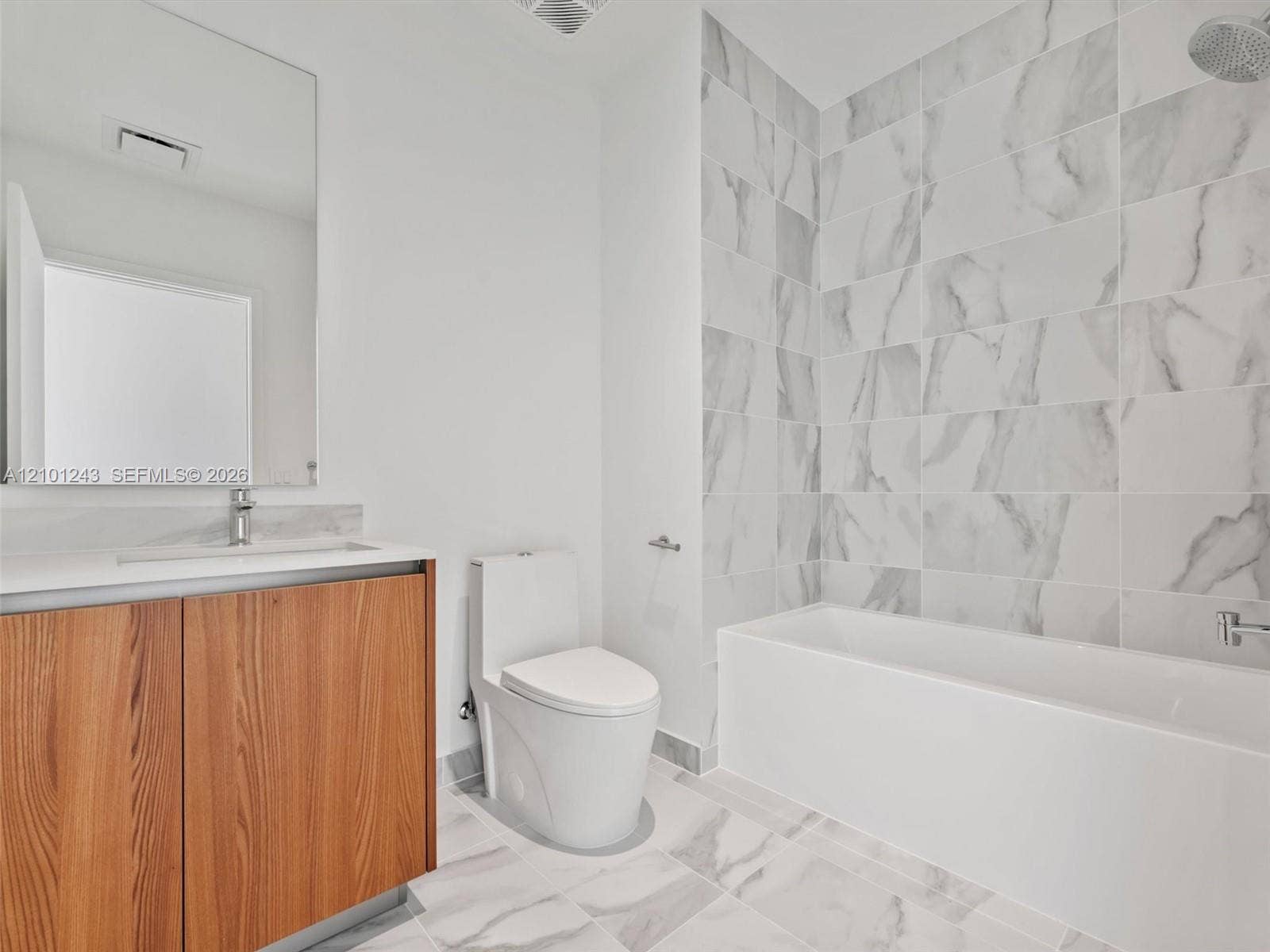 Bathroom featuring a wood-finish vanity with a stone-surface countertop, floor-to-ceiling tile shower surround, and large-format tile flooring