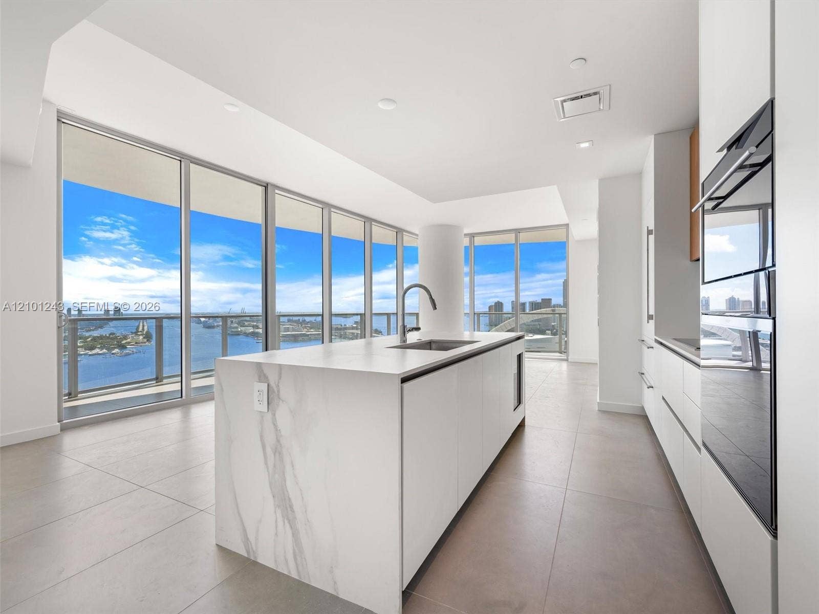 Kitchen featuring a central island with stone-finish waterfall edges, stainless steel under-mount sink, integrated appliances, floor-to-ceiling windows, and tile flooring