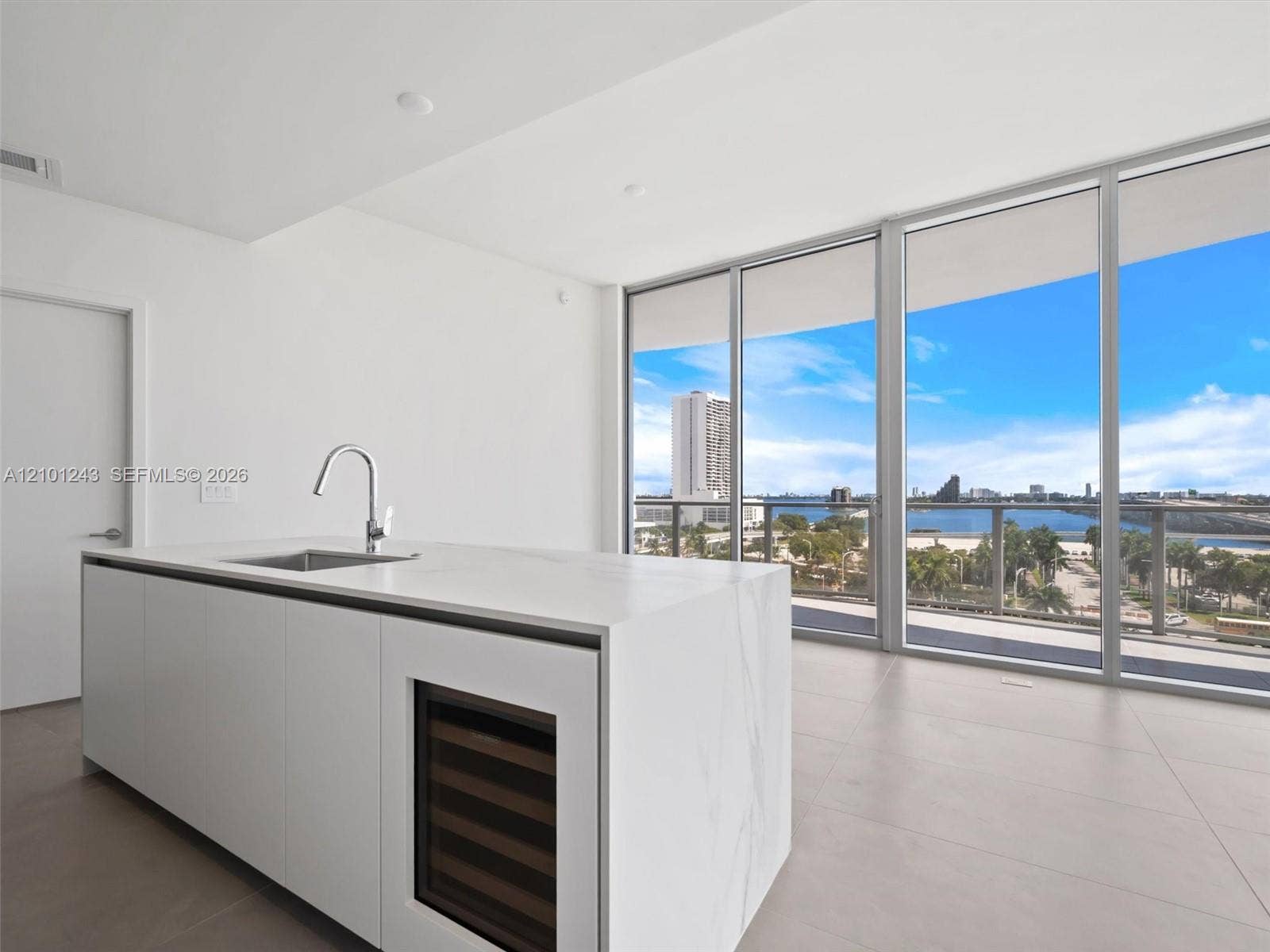 Kitchen island featuring stone-finish countertops, an undermount sink with a gooseneck faucet, integrated wine cooler, and floor-to-ceiling glass windows with water and skyline scenery