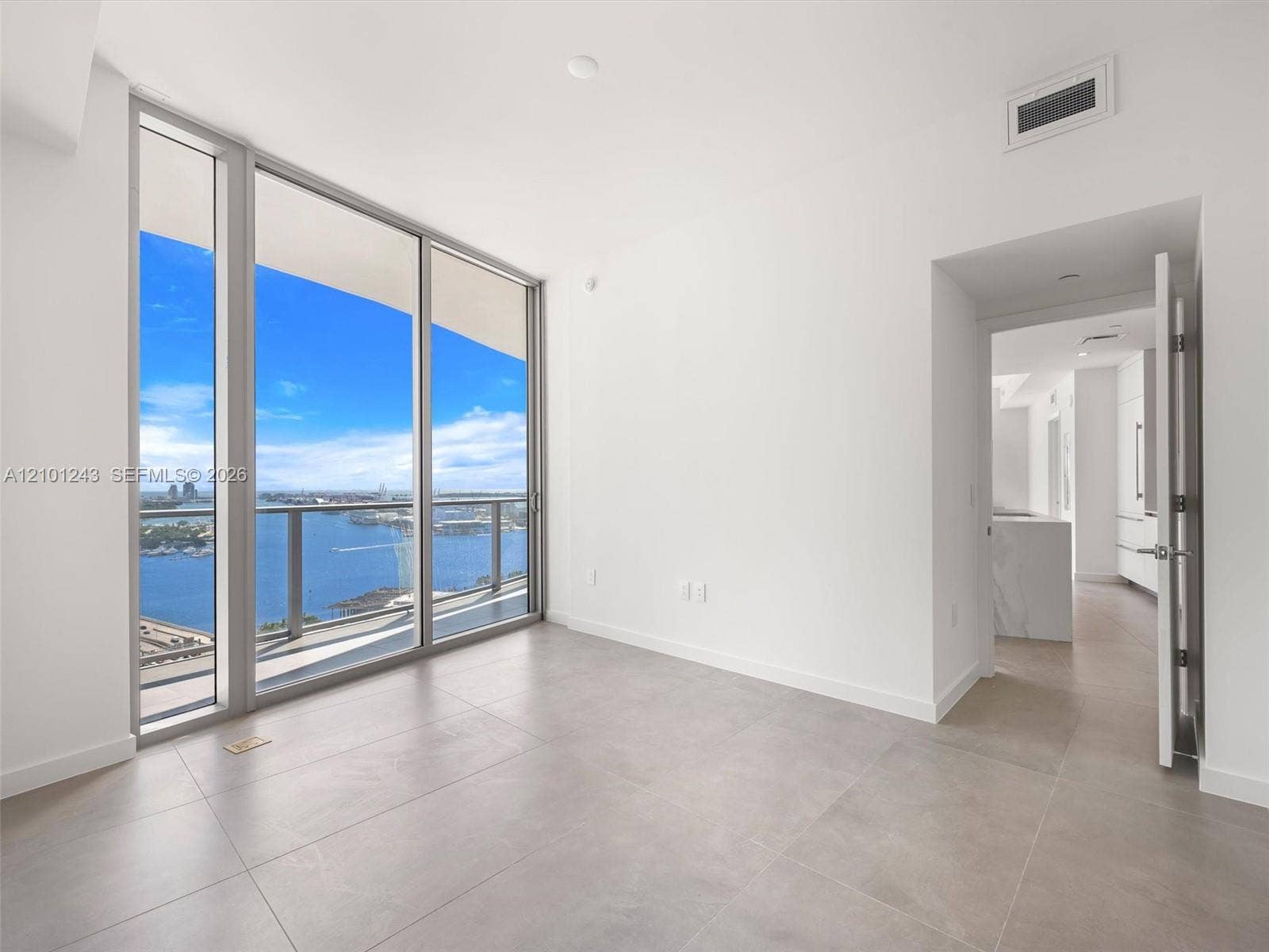 Floor-to-ceiling glass windows, private balcony, neutral tile flooring, and metal-framed sliding glass doors