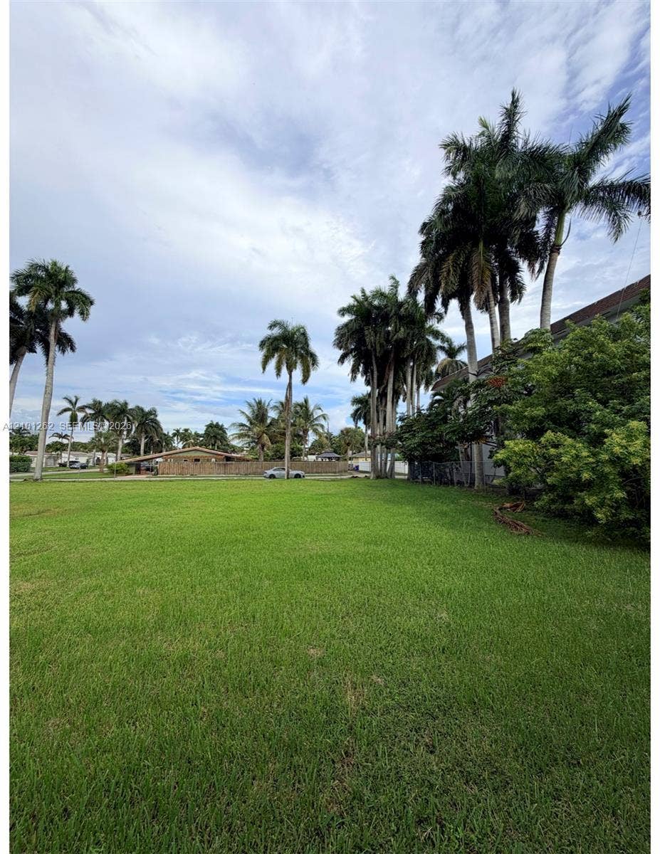 Expansive grass lawn featuring mature palm trees and established perimeter vegetation