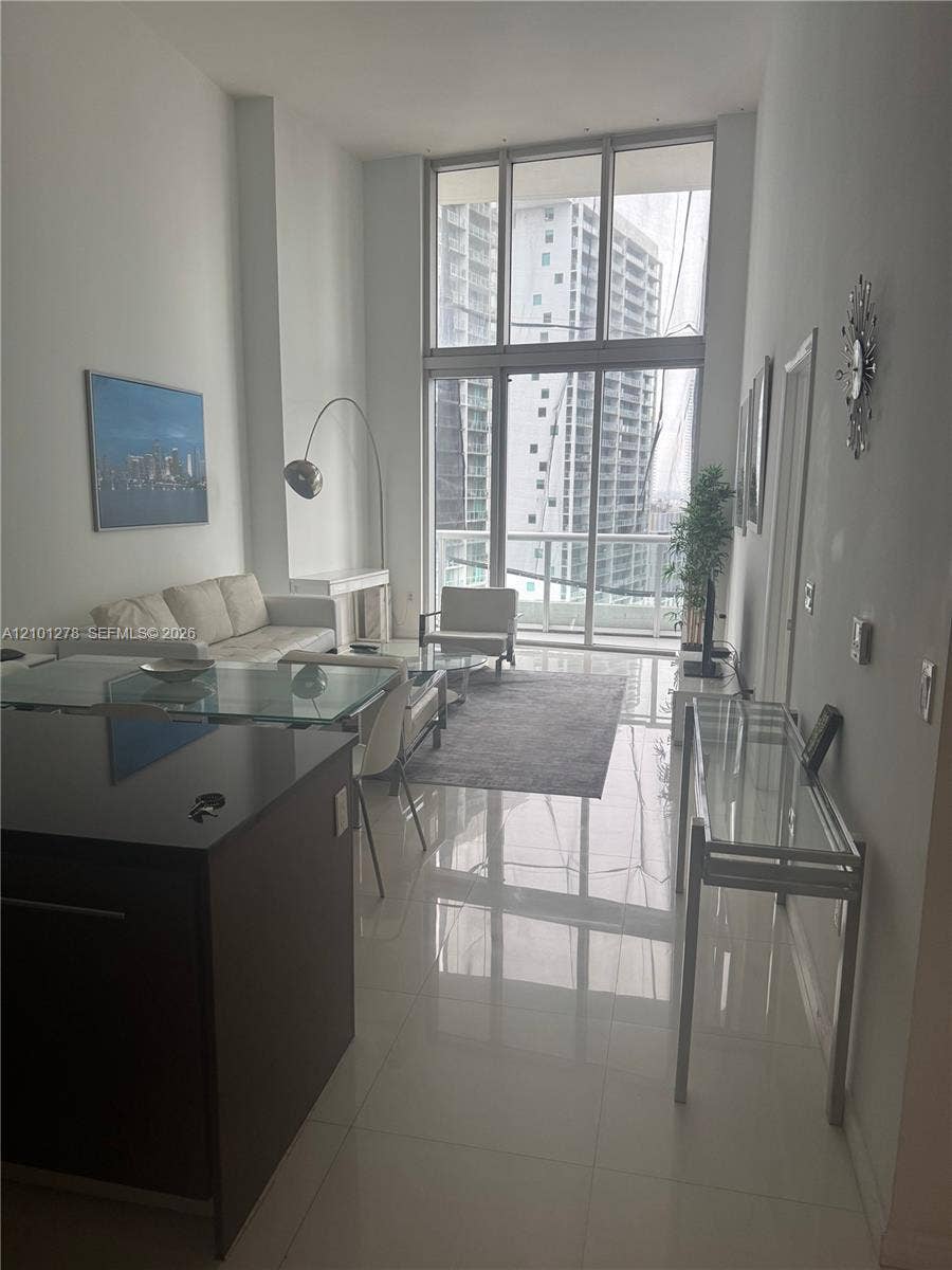 485 Brickell Avenue, #2806, Miami, Miami, FL 33131 Double-height floor-to-ceiling windows, polished tile flooring, glass-railed balcony, and dark-toned kitchen cabinetry