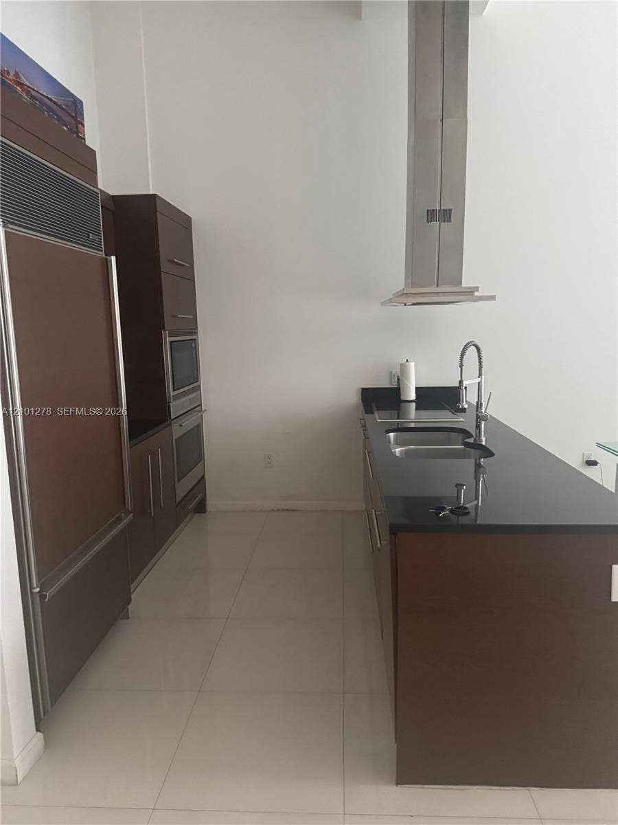 485 Brickell Avenue, #2806, Miami, Miami, FL 33131 Kitchen featuring custom wood cabinetry, dark stone countertops, stainless steel wall-mounted range hood, built-in double oven, and integrated refrigerator