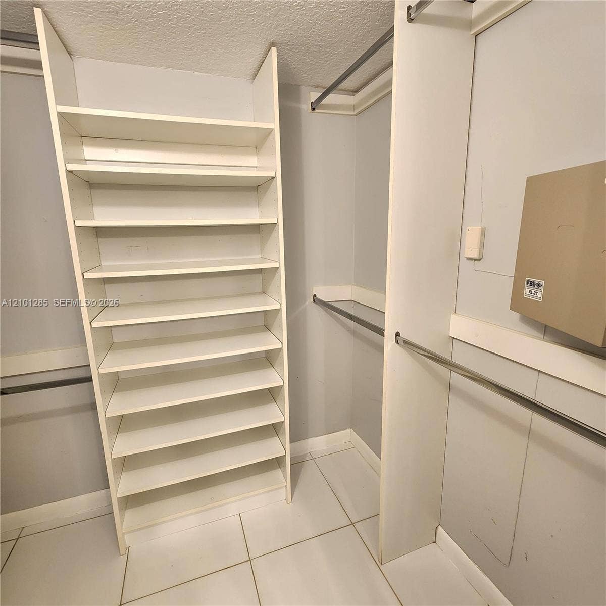 Custom walk-in storage featuring multi-level white shelving, horizontal metal hanging rods, and tile flooring