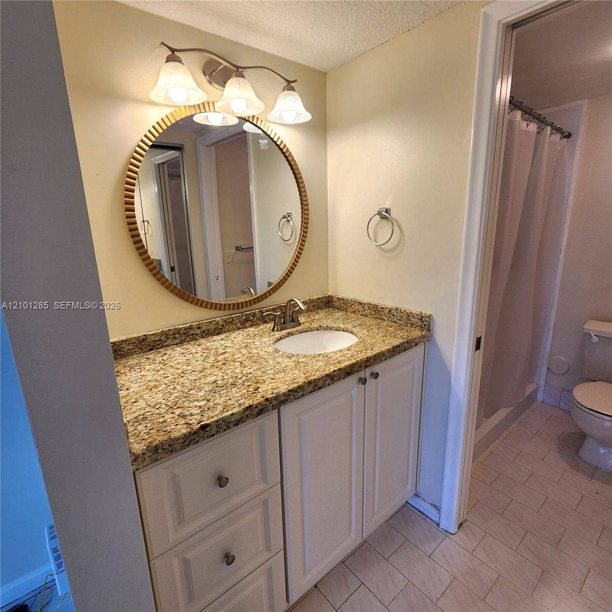 Vanity featuring a stone countertop, an oval under-mount sink, white cabinetry with drawers, a circular framed mirror, and a three-light fixture