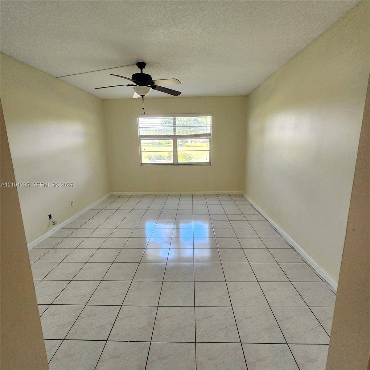 Room featuring neutral wall paint, white tile flooring, large horizontal window, and a ceiling fan with integrated lighting